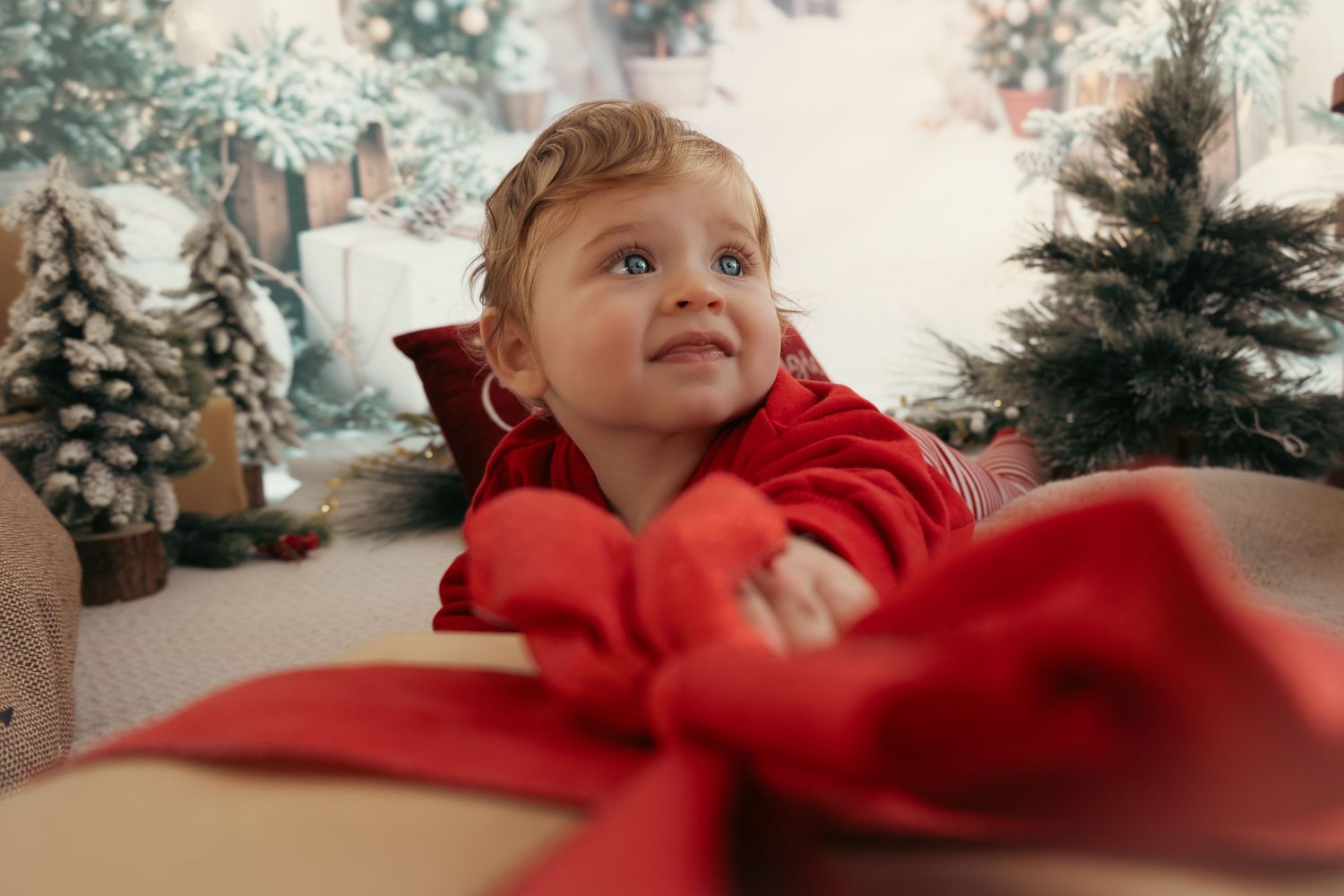 Child in red looks up excitedly at Christmas decorations and wrapped presents.