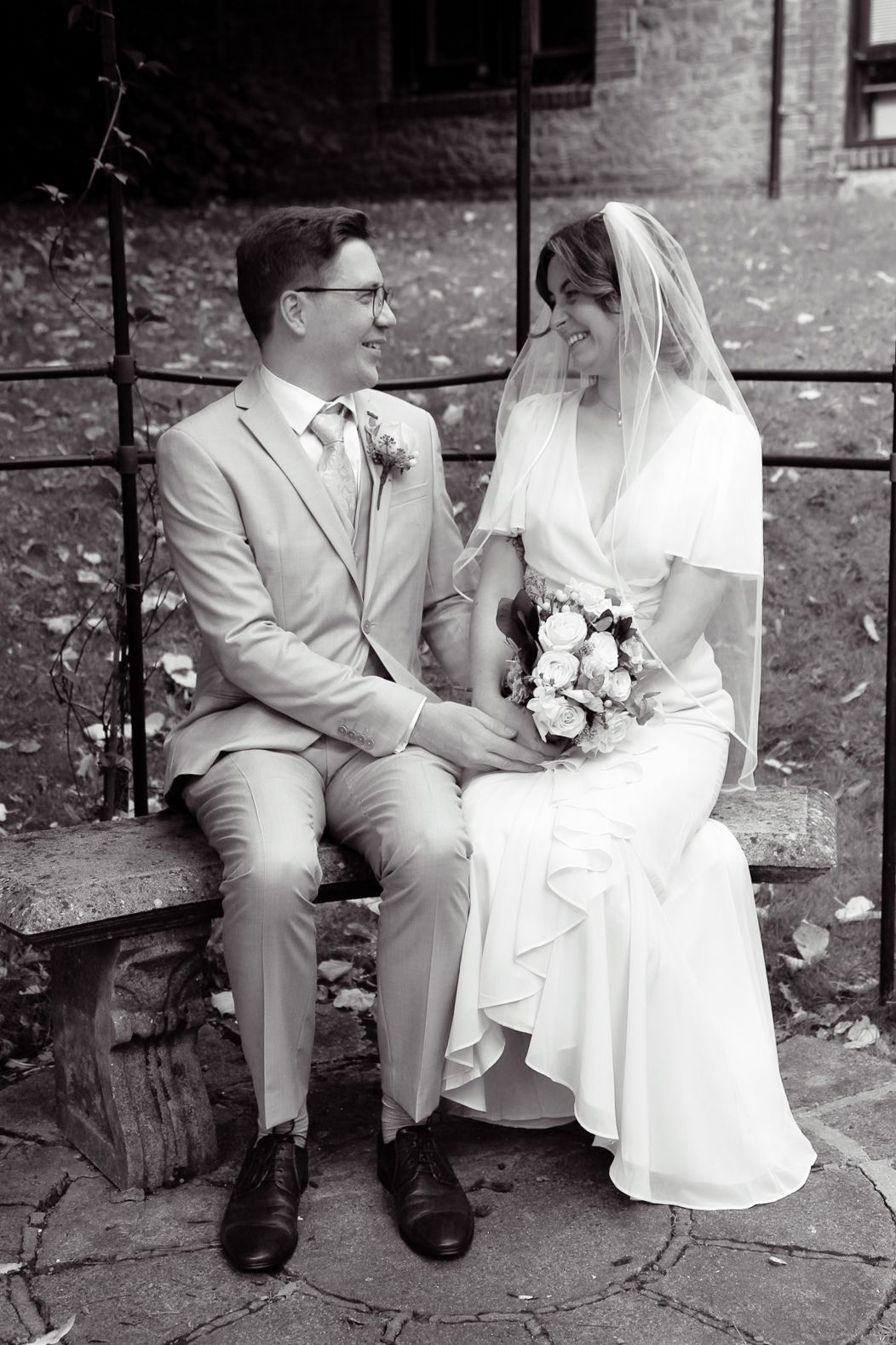 A black and white wedding photo of a couple sitting on a stone bench.