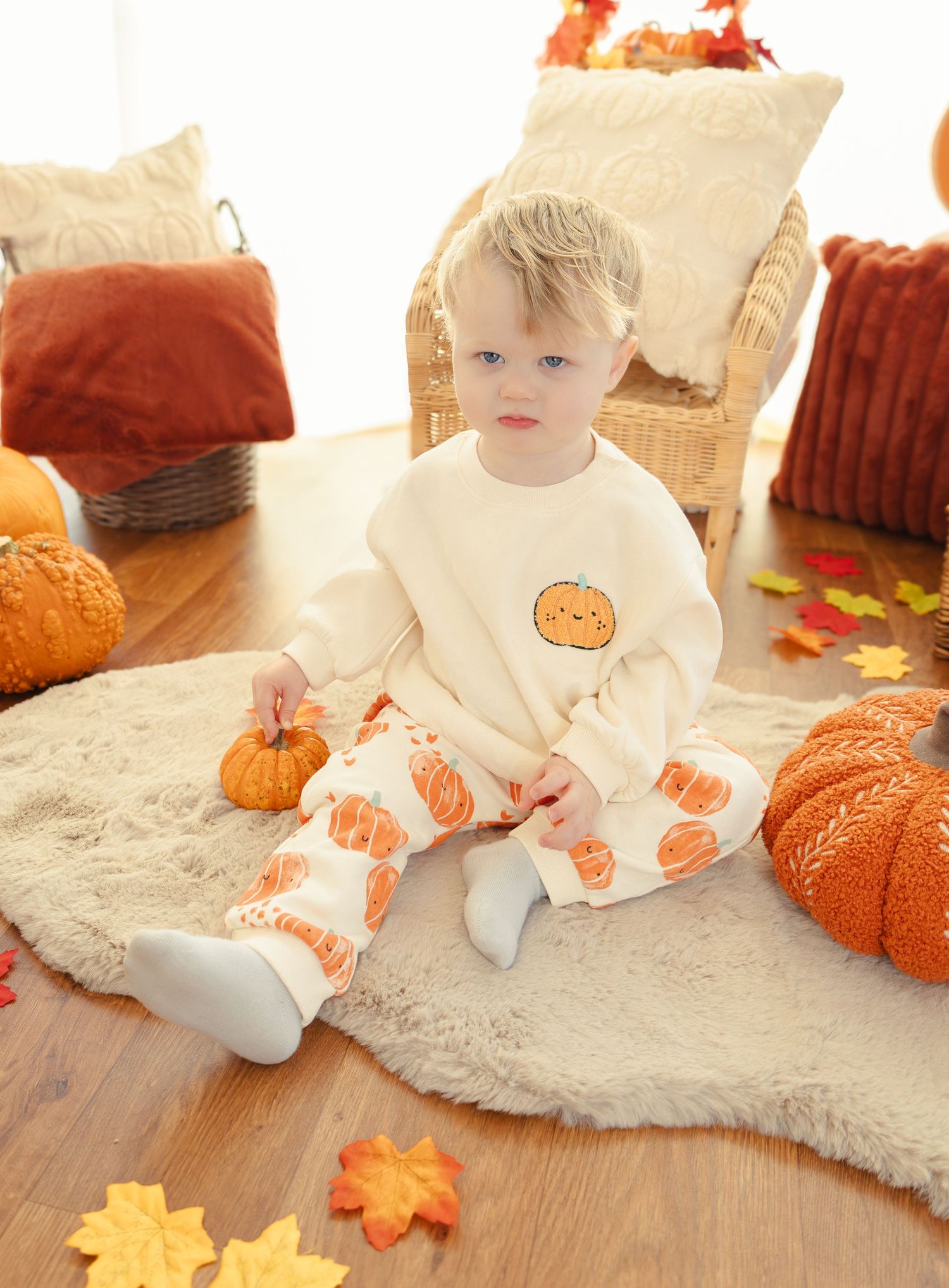 White dress with pumpkin pattern on cream carpet surrounded by fall decorations.