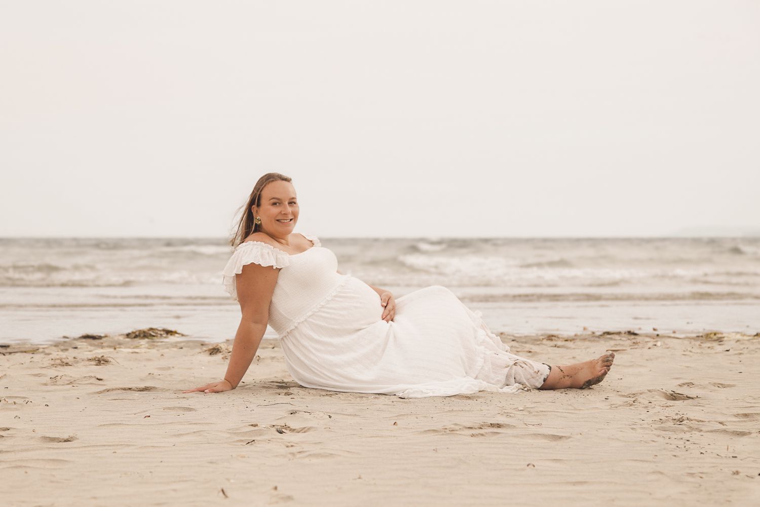 Person in white dress lying on sandy beach near ocean waves.