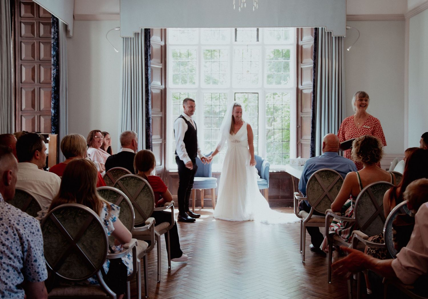 Wide shot of wedding ceremony setup in an elegant room with large windows.