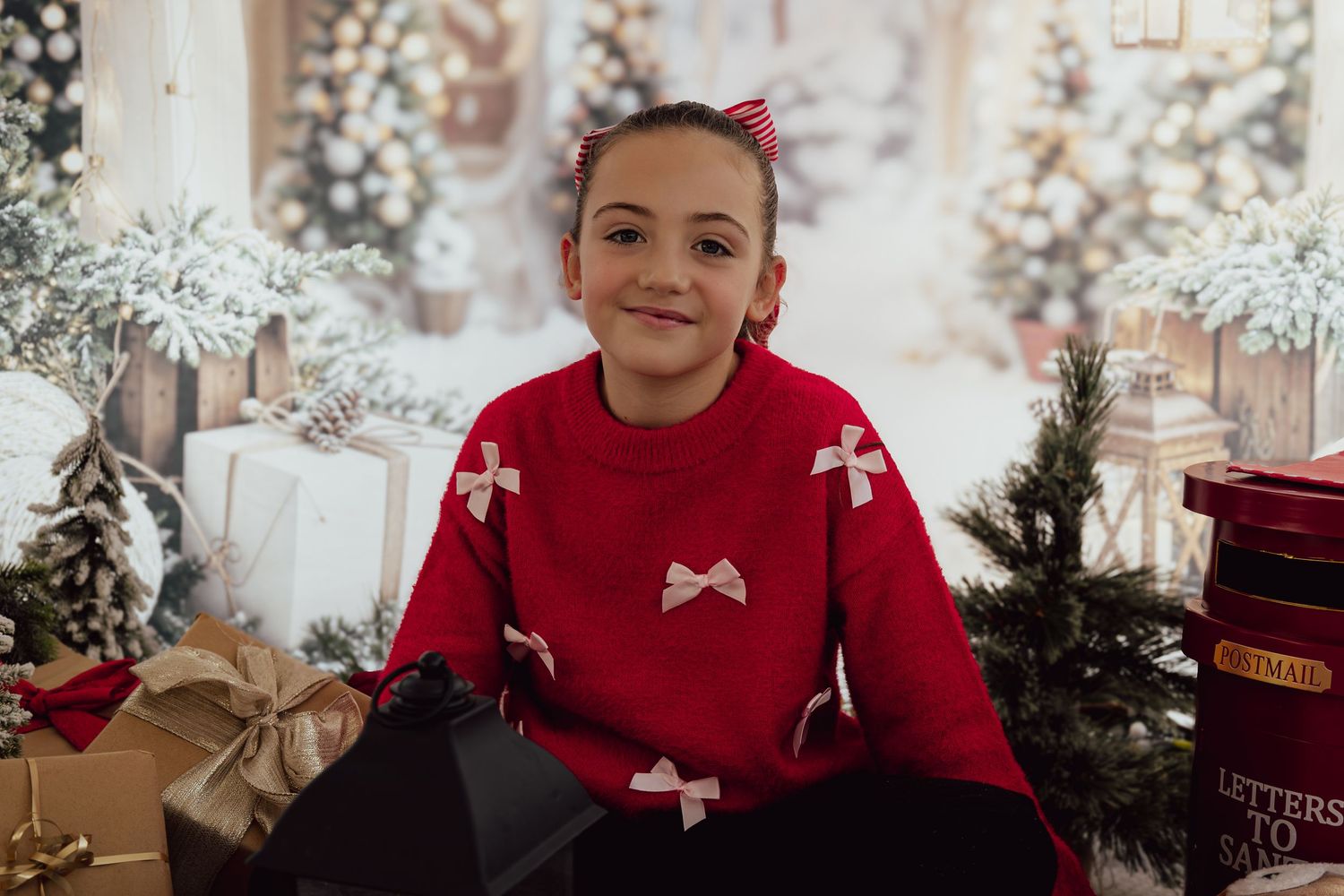 Person in red sweater with bow details smiles among Christmas decorations and presents.