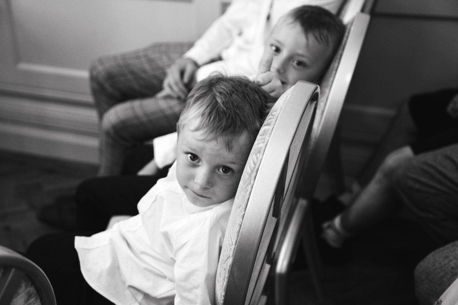 Two young boys in white shirts sit on chairs during a formal event.