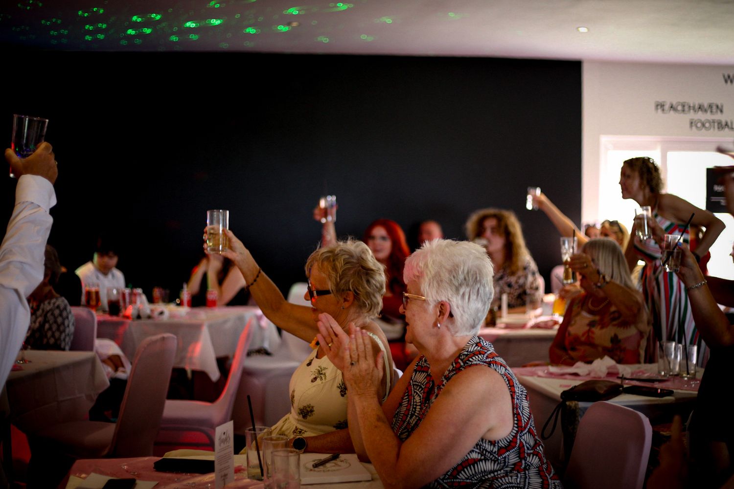 Wedding reception guests dance and celebrate in a dimly lit venue.
