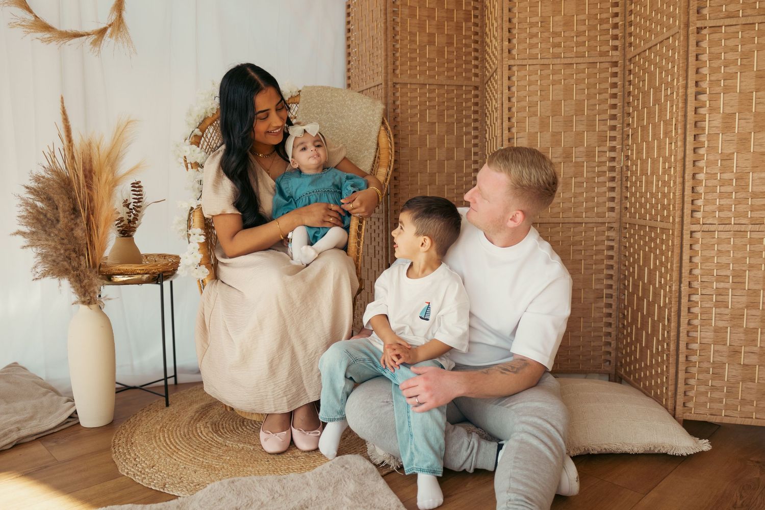 Happy family with mother, father, and two young children posing together in a cozy bohemian-styled living room.