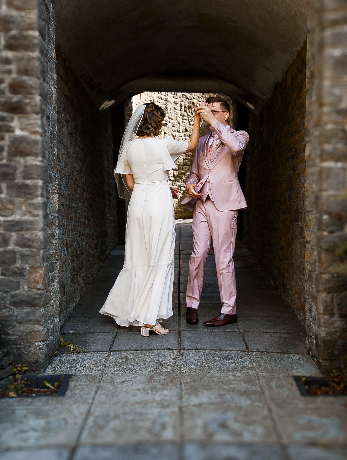 Wedding couple poses in a series of romantic shots within a stone tunnel passageway.