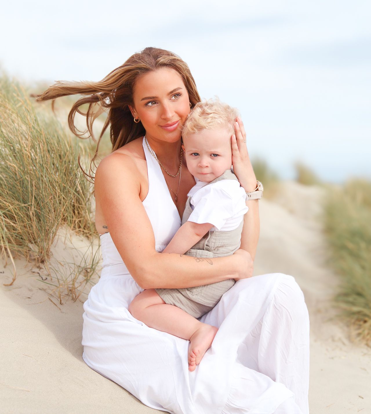 Parent and child share tender moments while sitting on beach sand dunes.