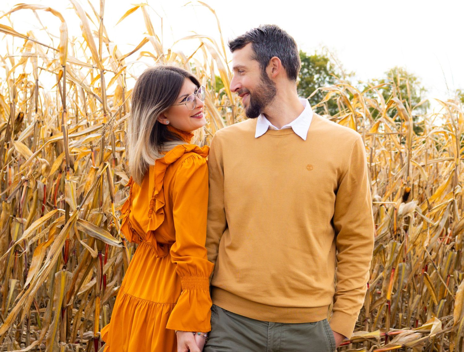 Couple in coordinated fall outfits sharing romantic moments in cornfield setting.