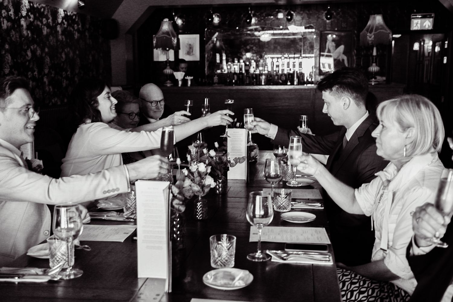 Wedding reception candid moments at a dimly lit bar with guests celebrating.