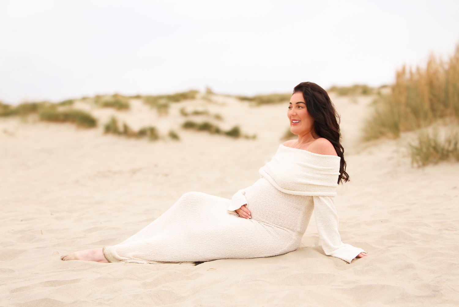 Person in cream colored dress reclines on sandy beach dunes.