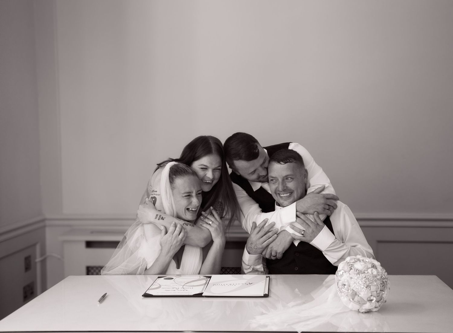 A group leans in together while signing documents at a white table.