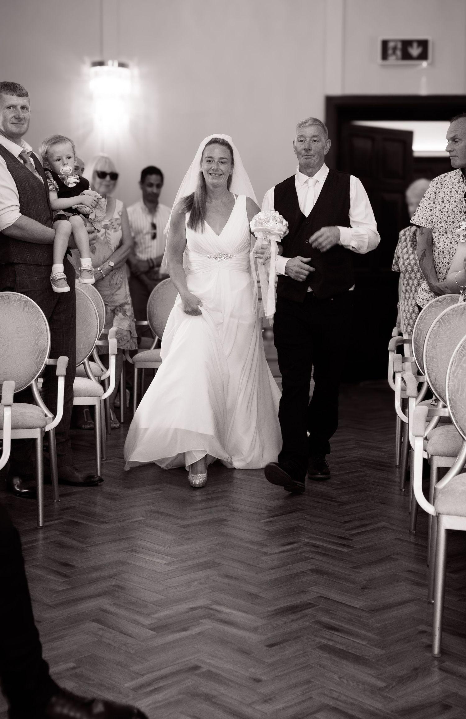 Wedding guests dance and celebrate on a herringbone wood floor at a reception.