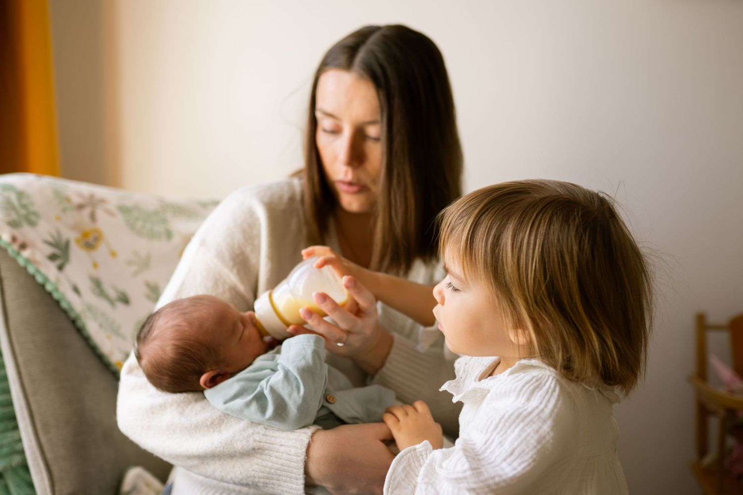 seance photo famille naissance et une enfant qui donne le biberon a son petit frère
