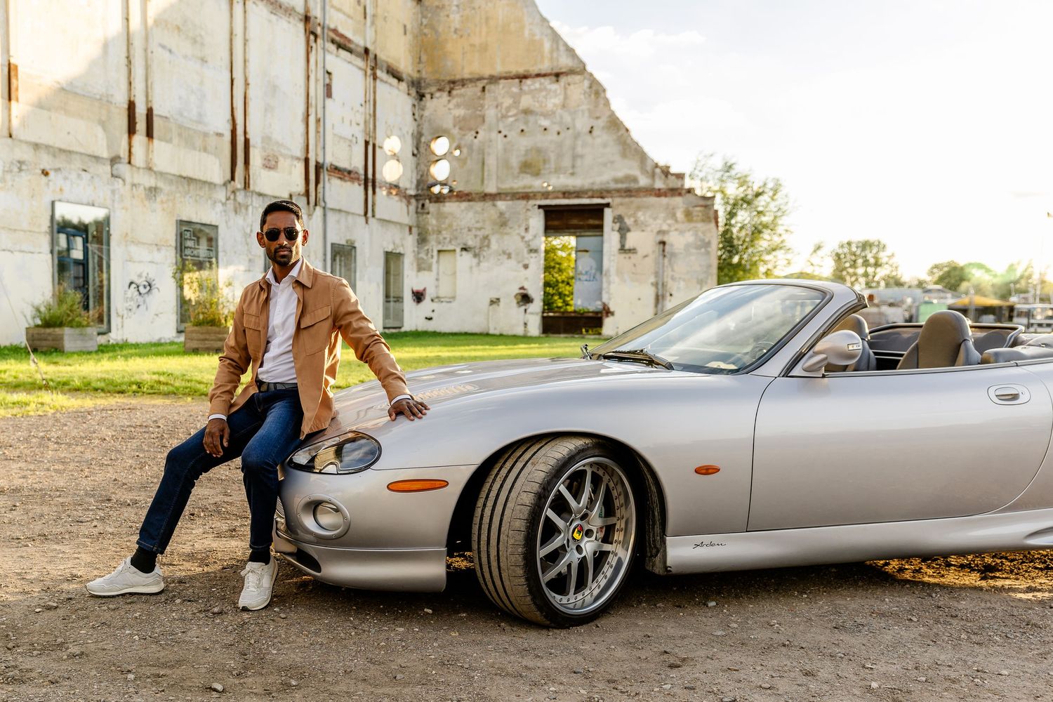 Casual clothing business man sitting on the hood of his car wearing sunglasses and white shoes