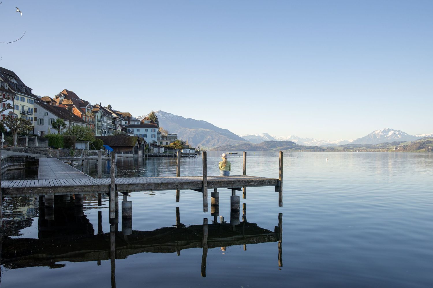 Woman sits on a pier looking into the distance where the mountains are