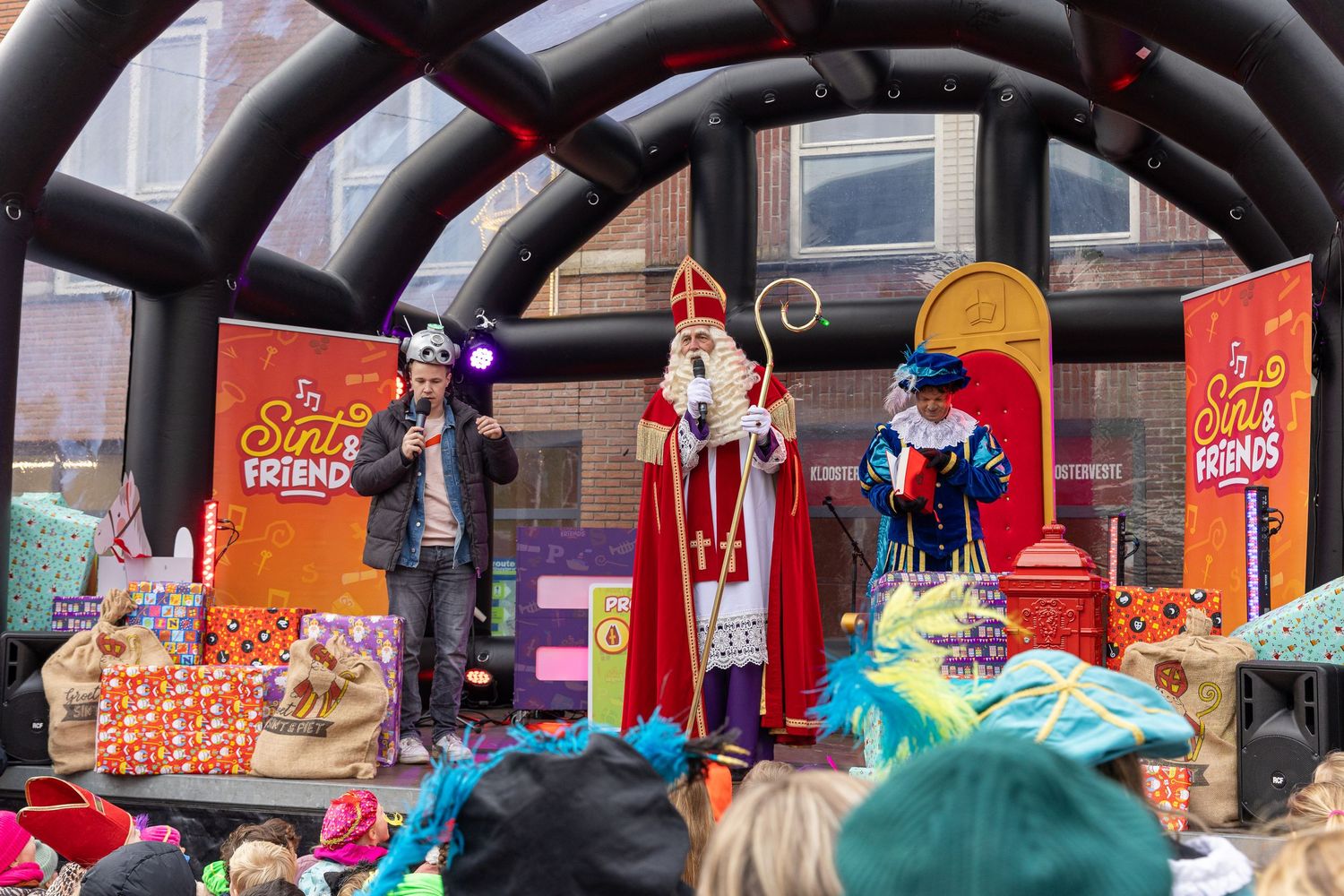 Sinterklaas addresses the audience from the stage, which is decorated with gifts.