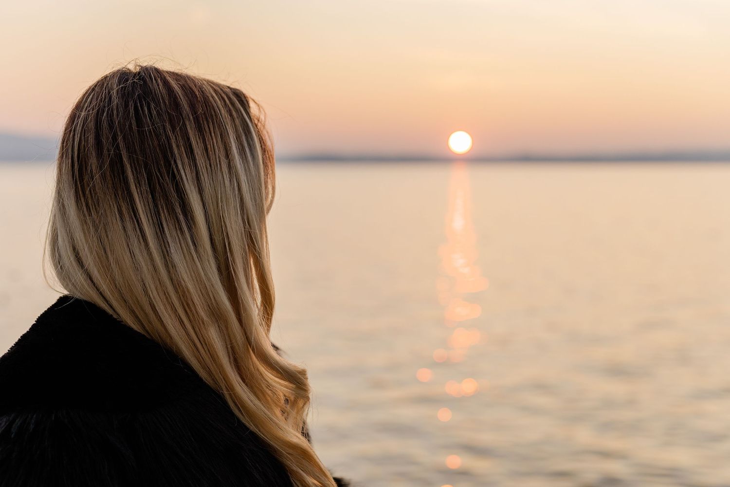 A beautiful sunset with reflections on the water and on the left side the back of a woman