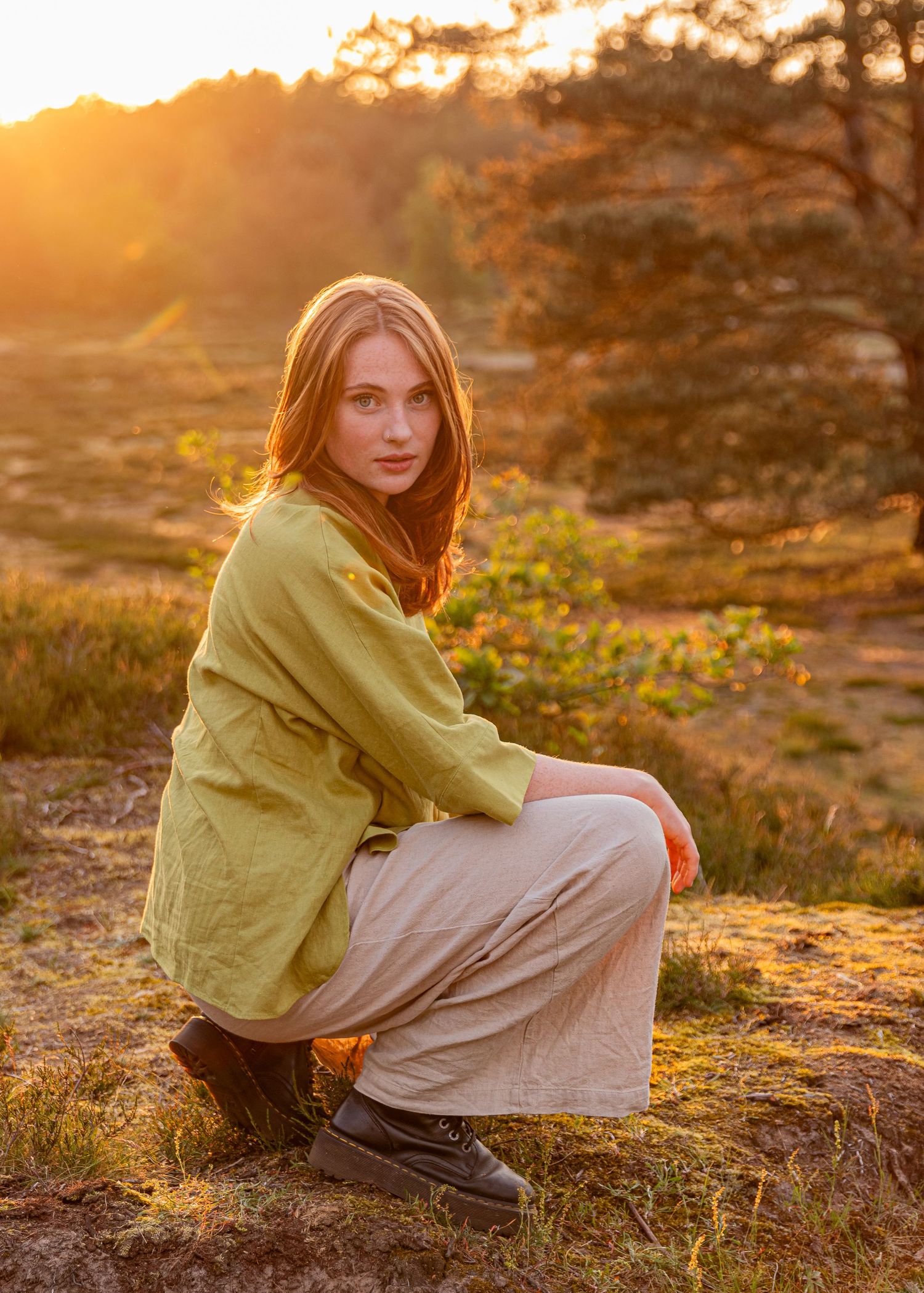 Young woman squats in loose clothing with the sunset in the background during a lifestyle golden hour session