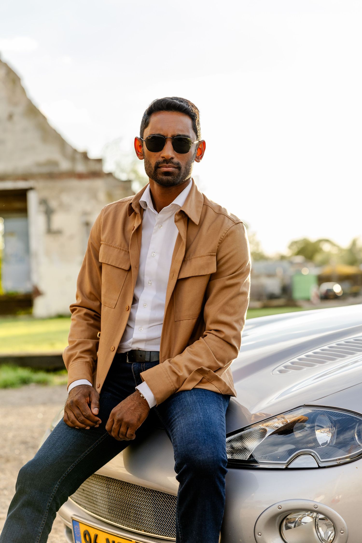 Casual clothing business man sitting on the hood of his car wearing sunglasses