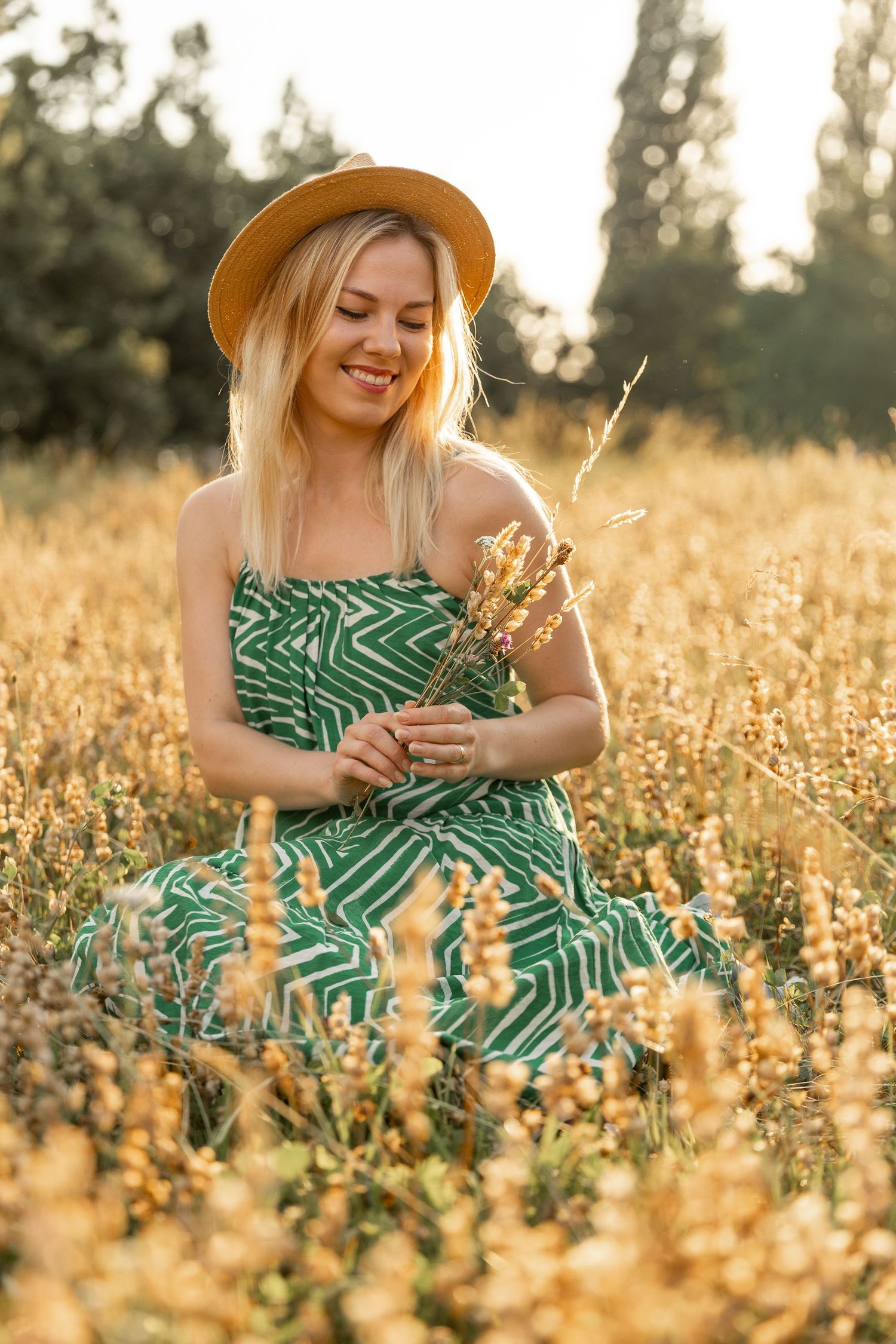 Woman wearing a summer hat sitting in a field of flowers while holding a few flowers in her hands