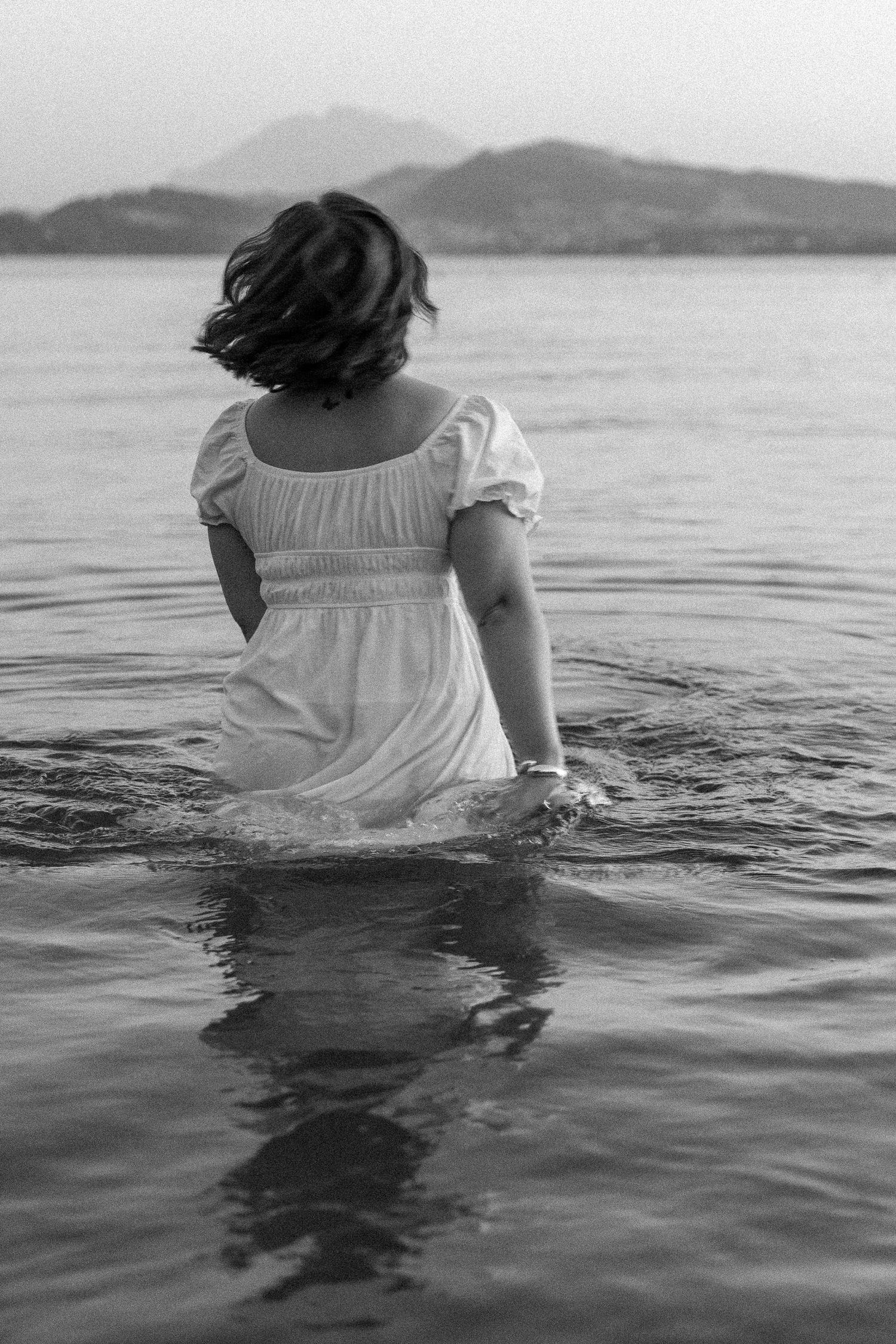 Black and white photo of a woman playing in the water wearing a white dress