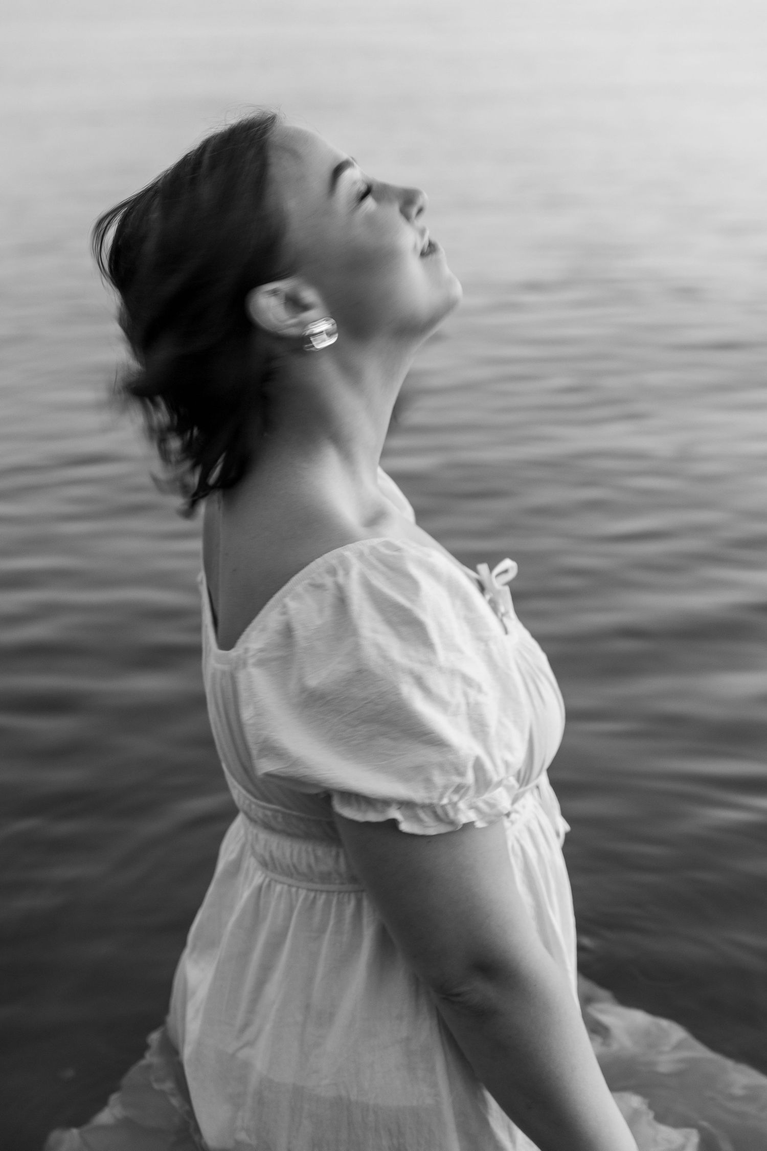 A black and white photograph of a woman in a white dress in the lake during golden hour