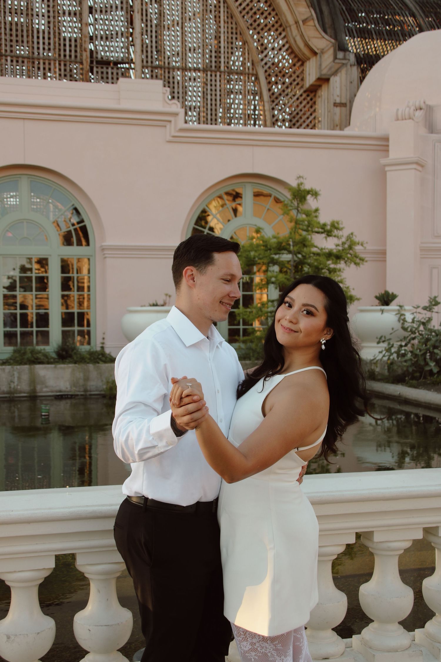 Couple dancing and smiling together against backdrop of classical architecture and reflecting pool.