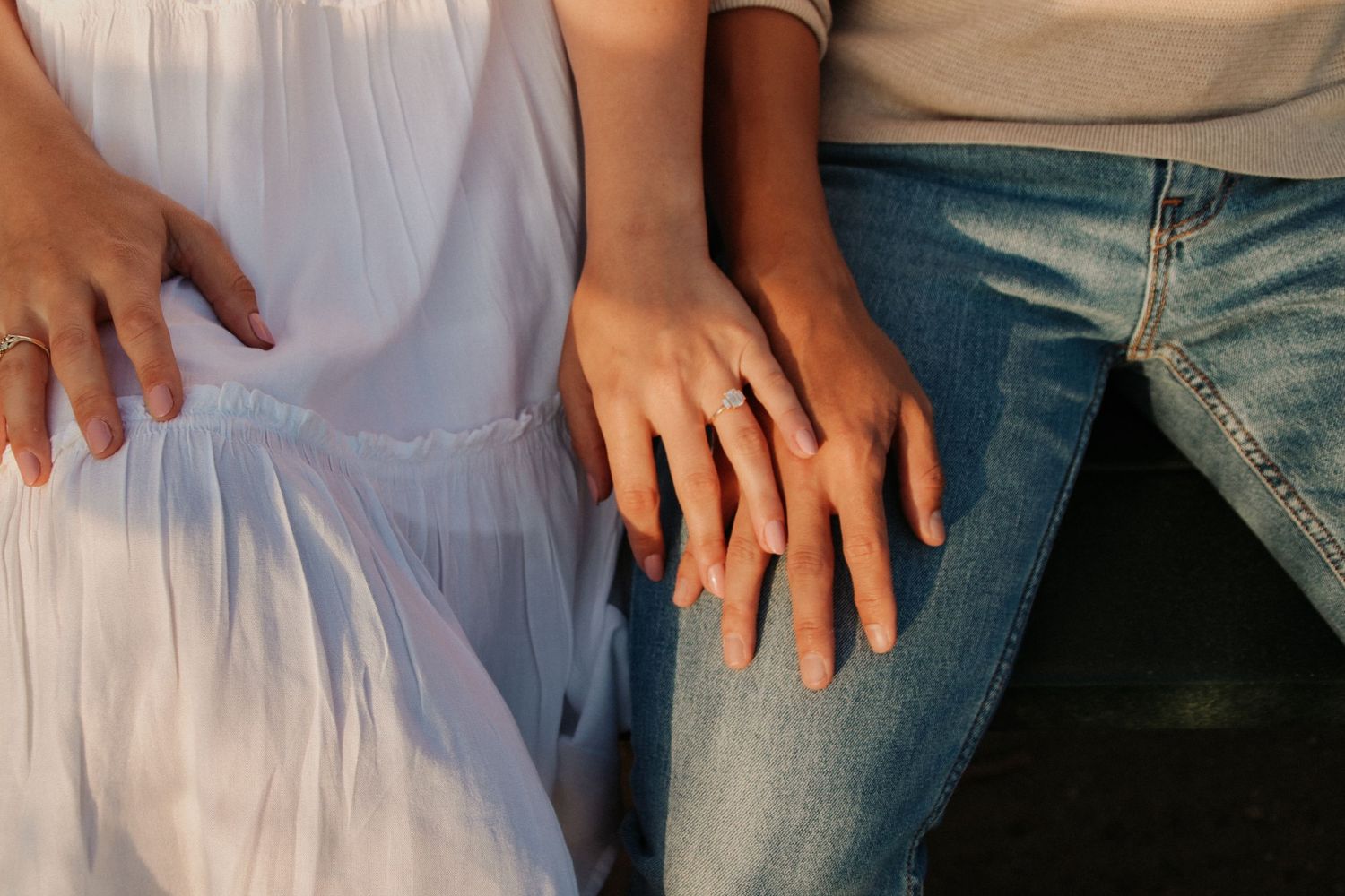 Close-up of hands resting on denim and white fabric showing intimate connection.