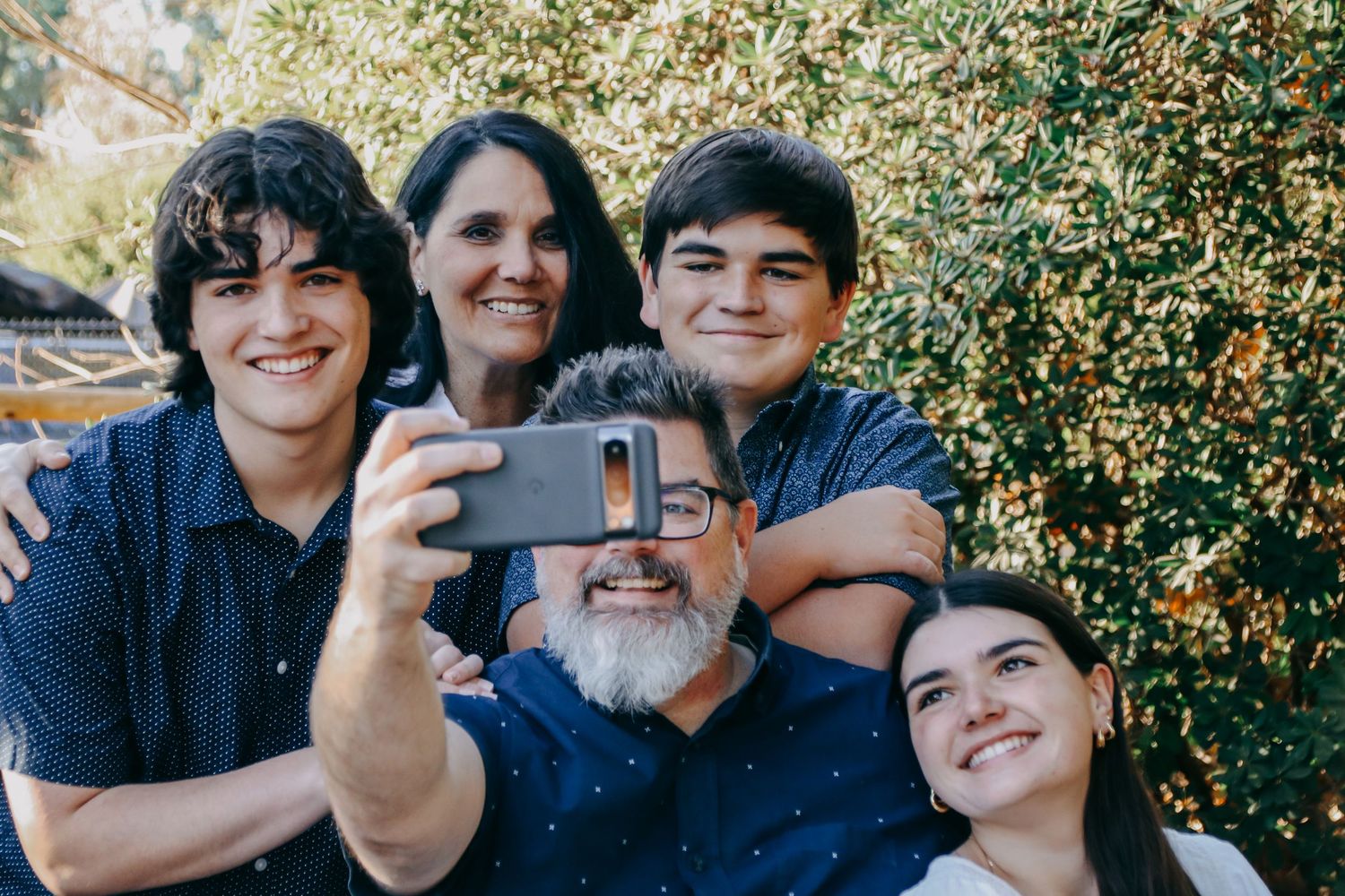 Candid outdoor portrait session with family members smiling together against trees.