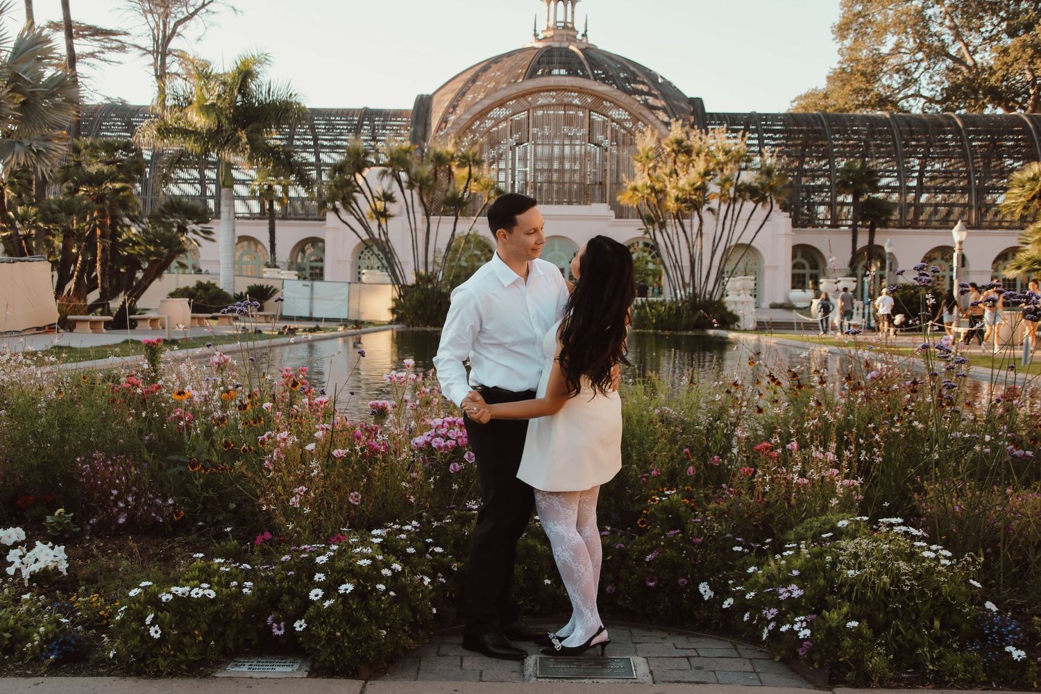 A tender moment captured between a couple in front of a stunning botanical building with garden landscaping.
