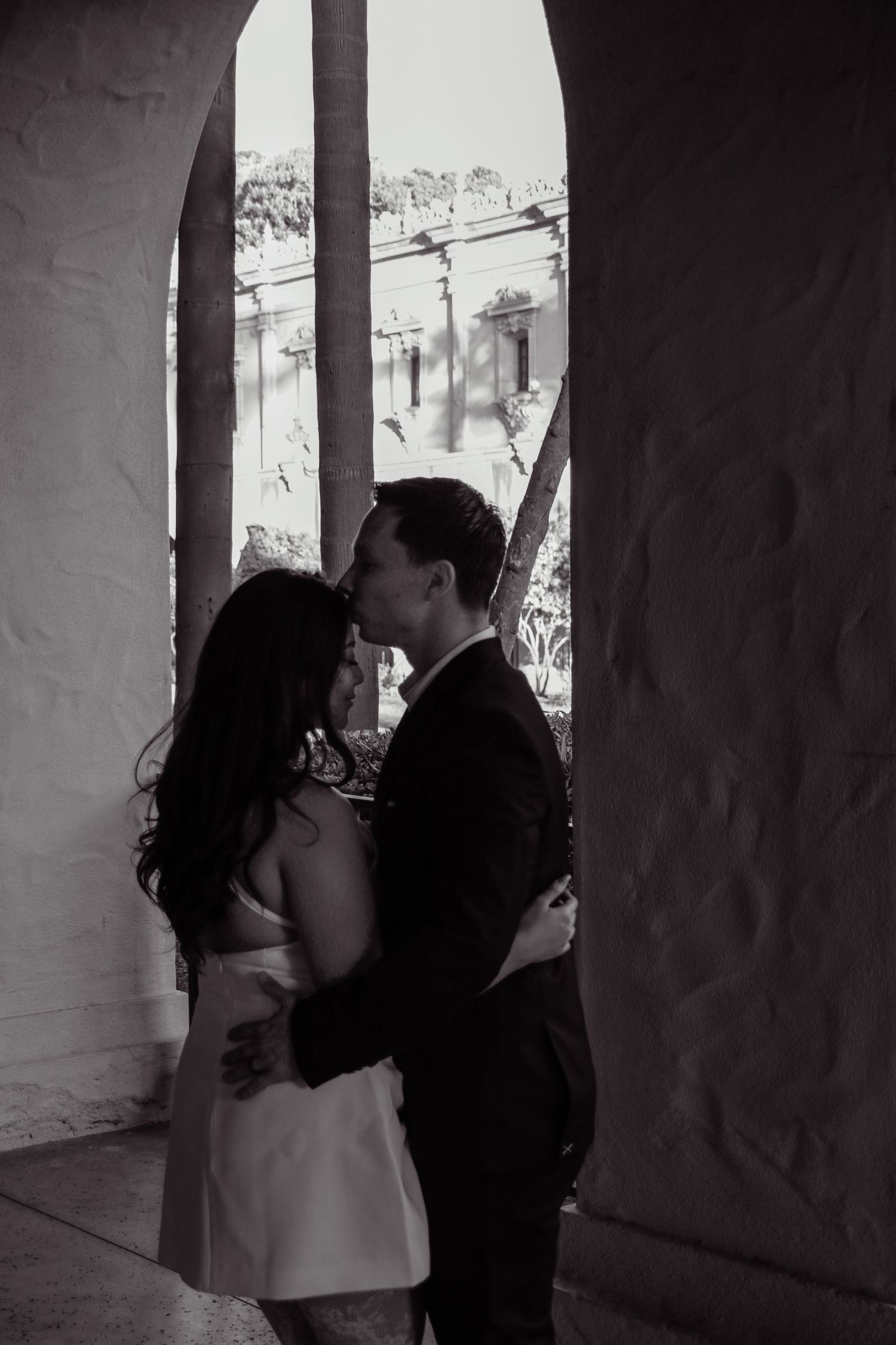 Black and white photo of intimate moment between couple framed by stone archway.