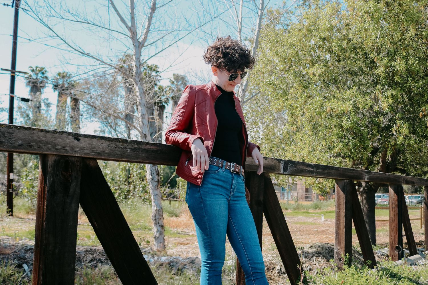 Fashion editorial composition with wooden bridge and natural foliage backdrop.