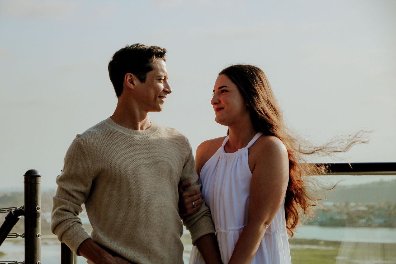 A joyful couple shares laughter together on an outdoor deck with wind blowing through their hair.