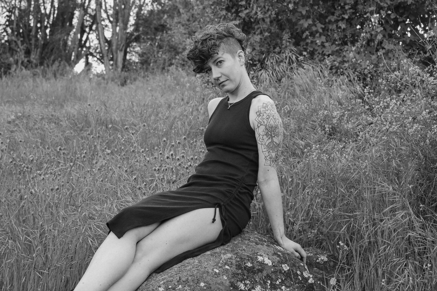 Person in black dress sits on rock surrounded by wildflowers and tall grass.