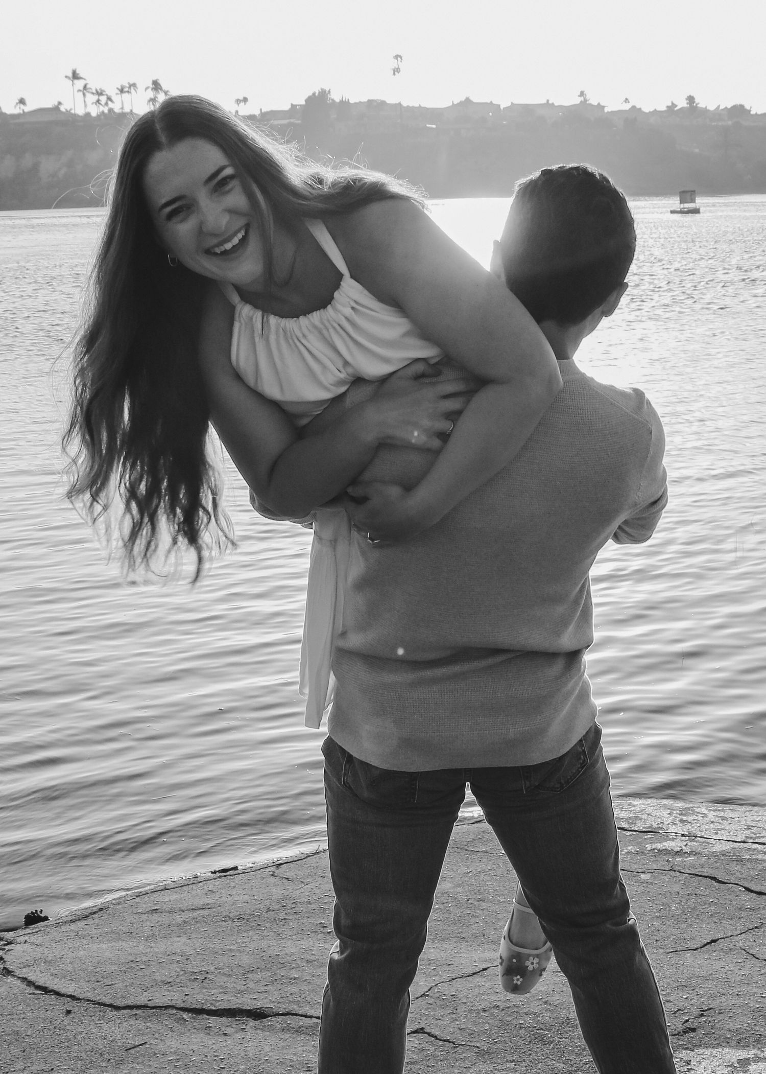 A black and white photo showing a playful moment between a couple at sunset.