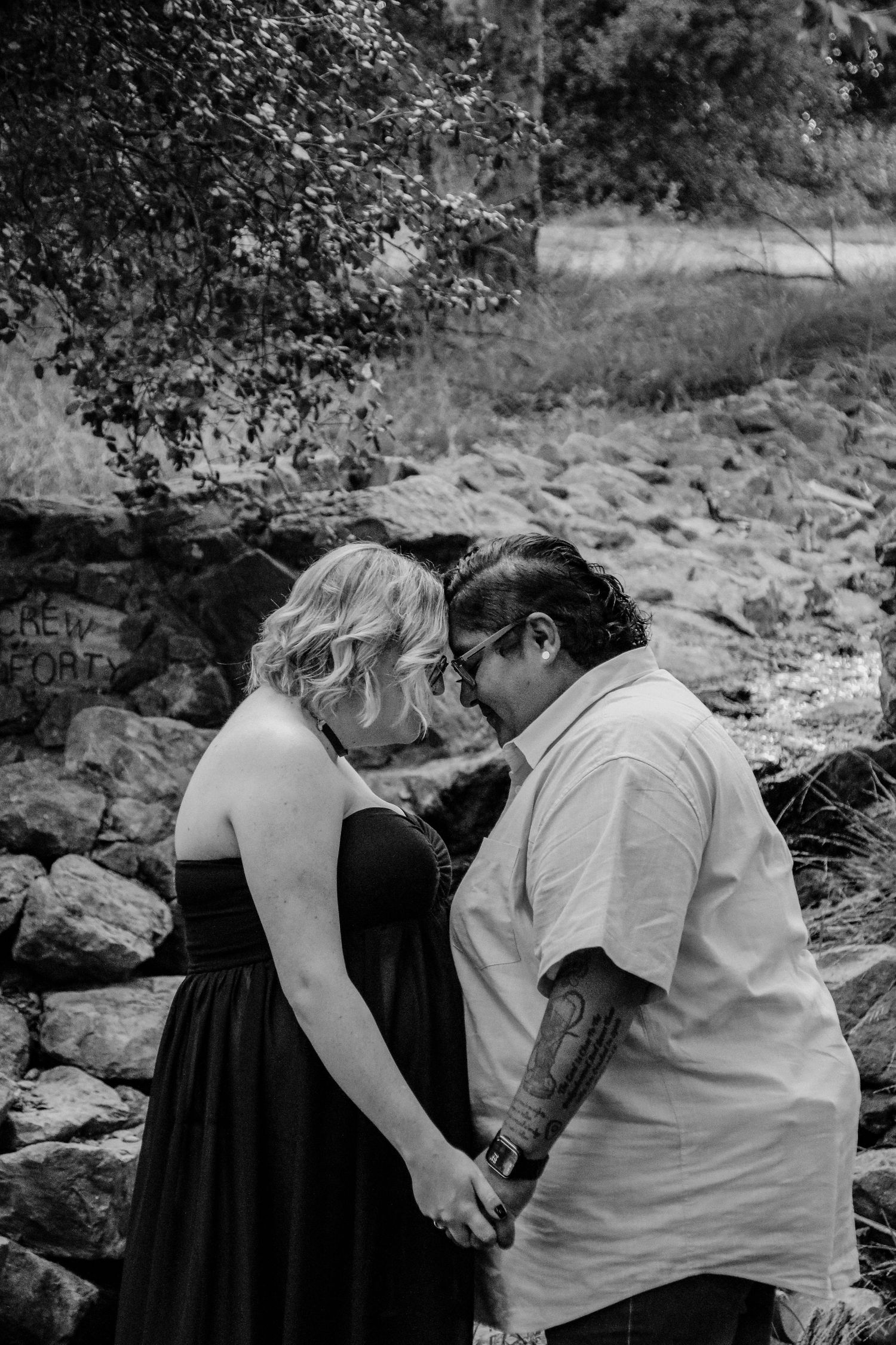 Intimate black and white portrait showing a tender moment between two people in a natural outdoor setting.