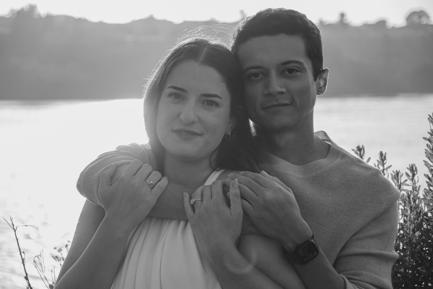 Black and white portrait of couple embracing by lakeside with soft lighting.