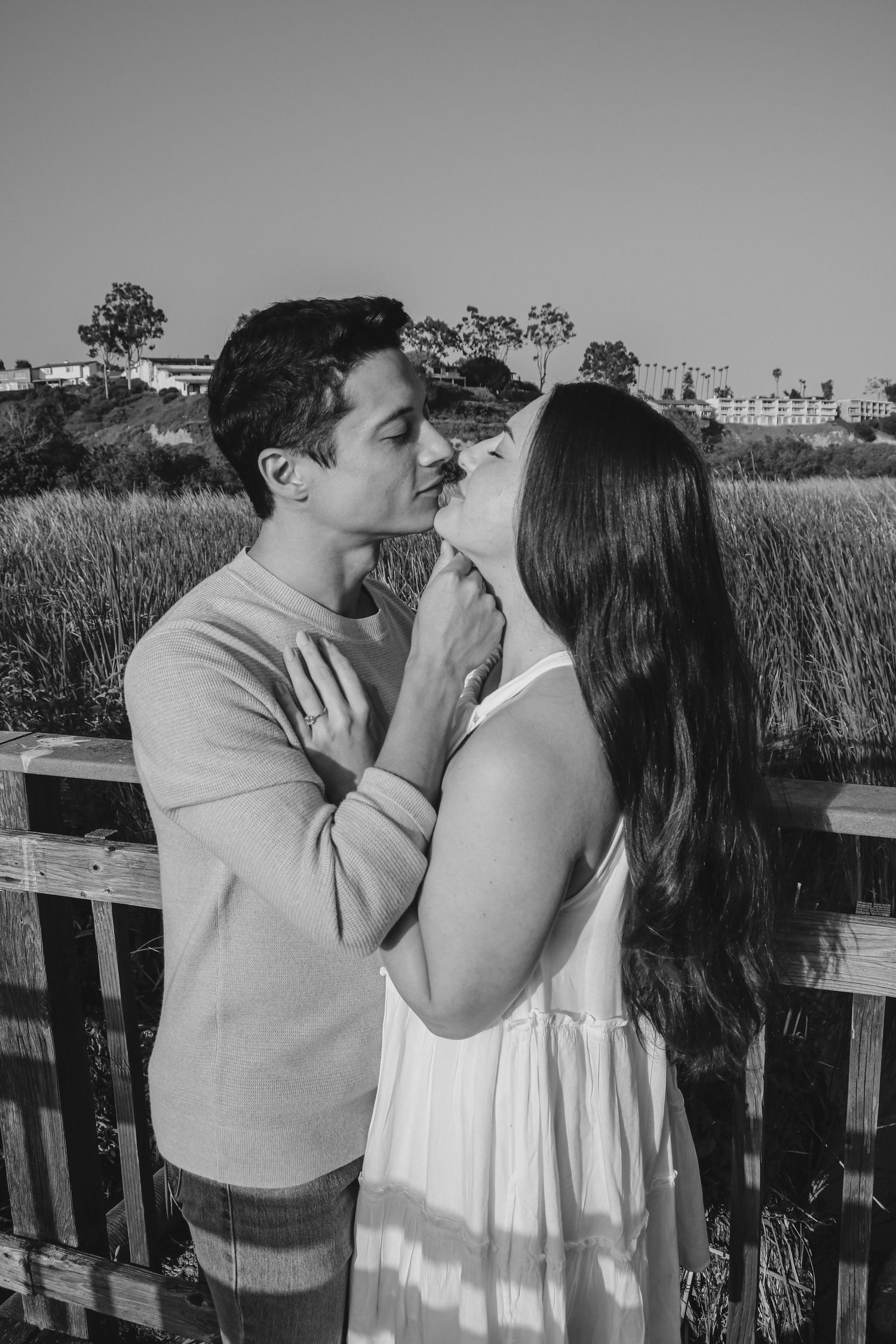 Monochrome capture of couple in gentle embrace with coastal scenery behind them.