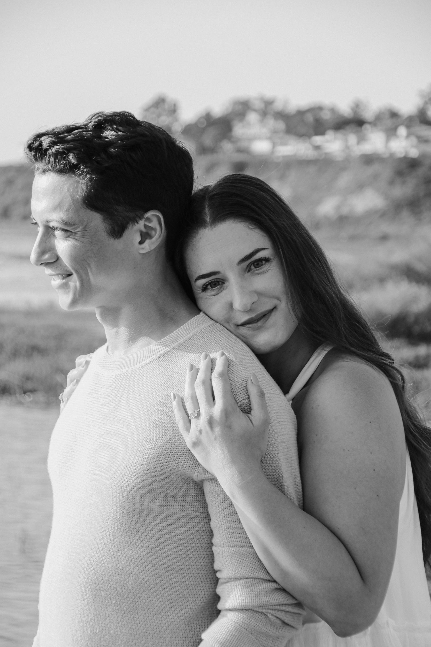 Romantic black and white portrait of a couple embracing outdoors by the water.