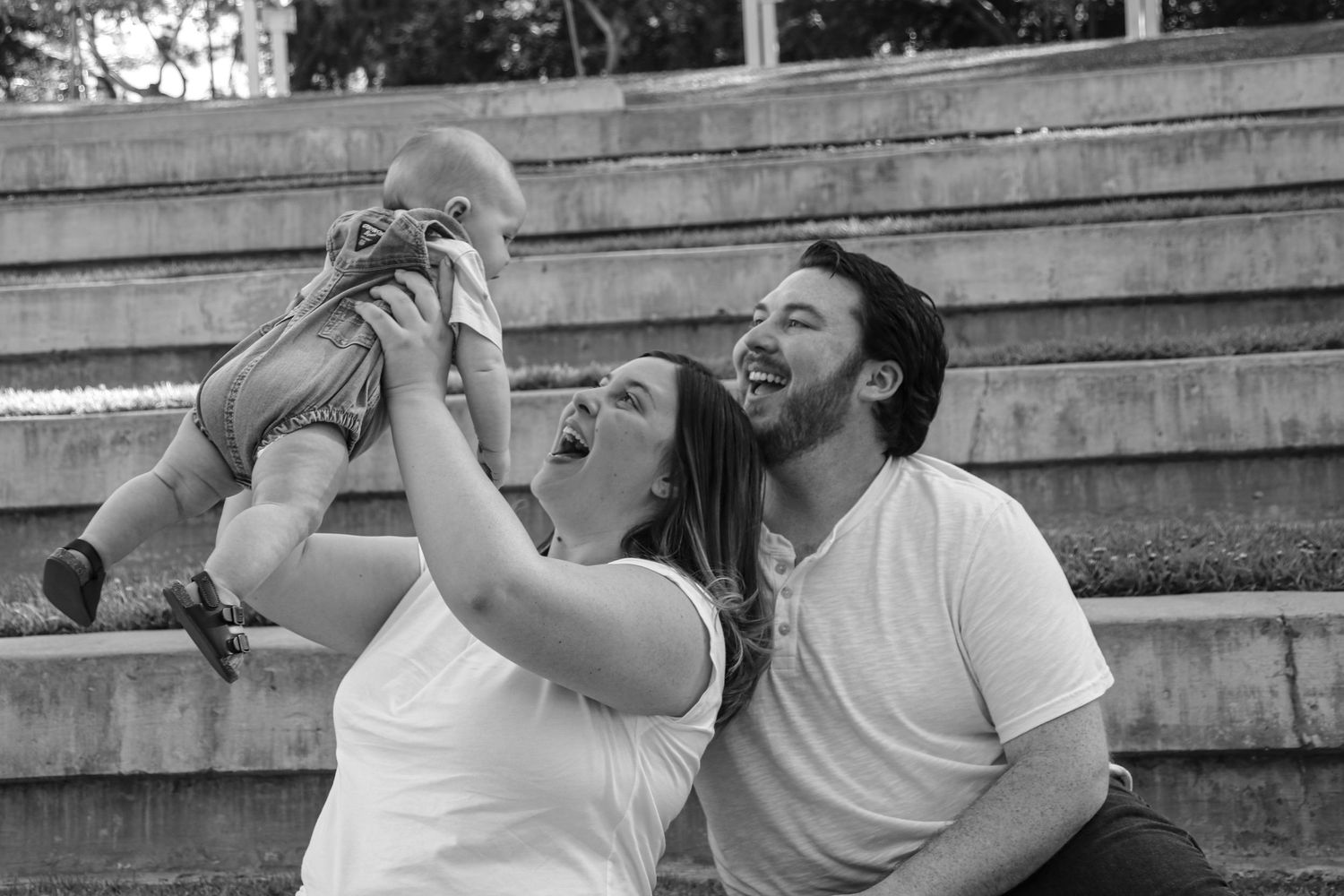 Family shares candid outdoor moments together sitting on concrete steps in matching white outfits.