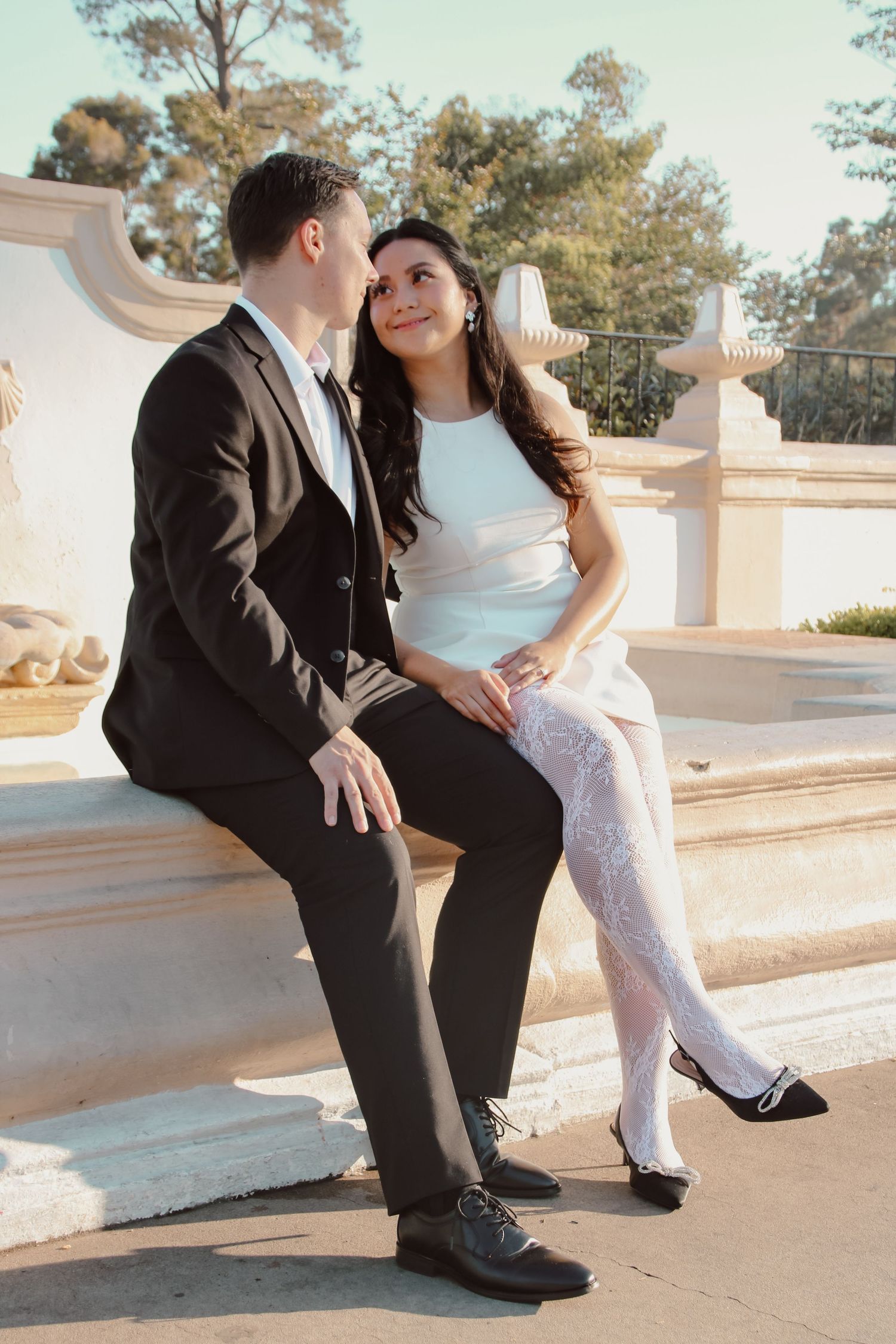Romantic couple in wedding attire shares playful moments on architectural steps in soft lighting.