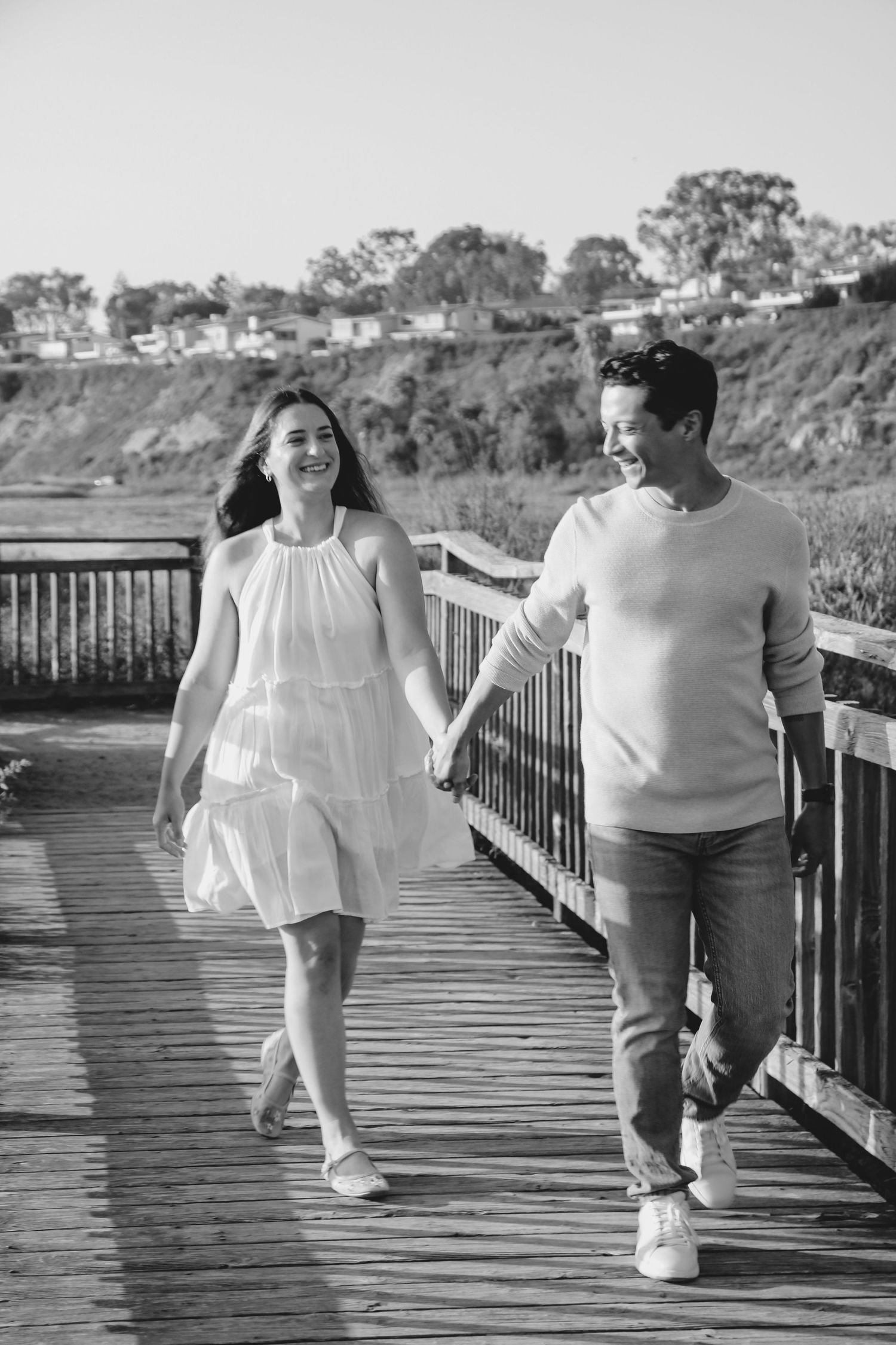 Black and white image of two people sharing playful moments on a coastal boardwalk.
