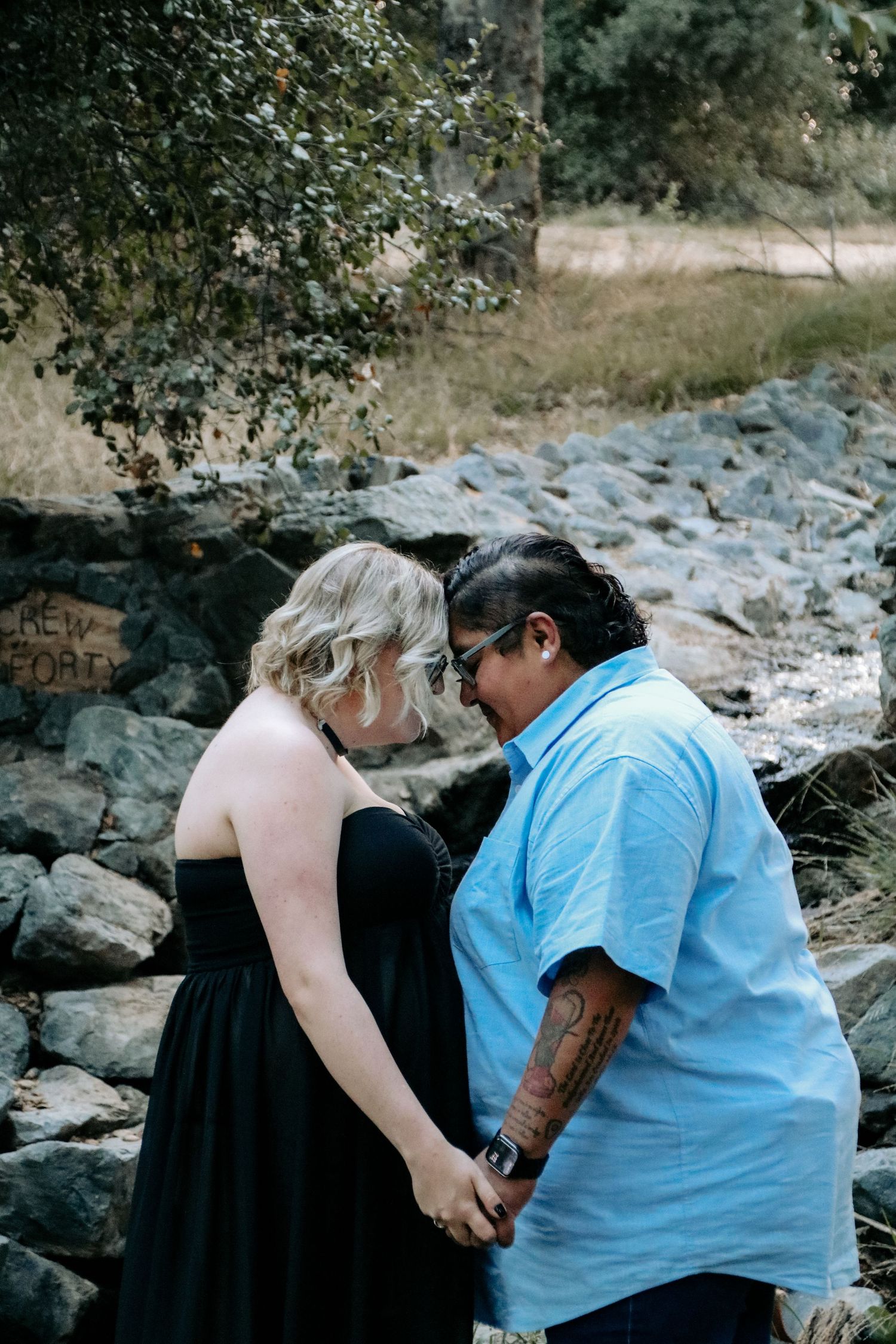 Two individuals share an intimate moment among rocky terrain in a natural outdoor setting.