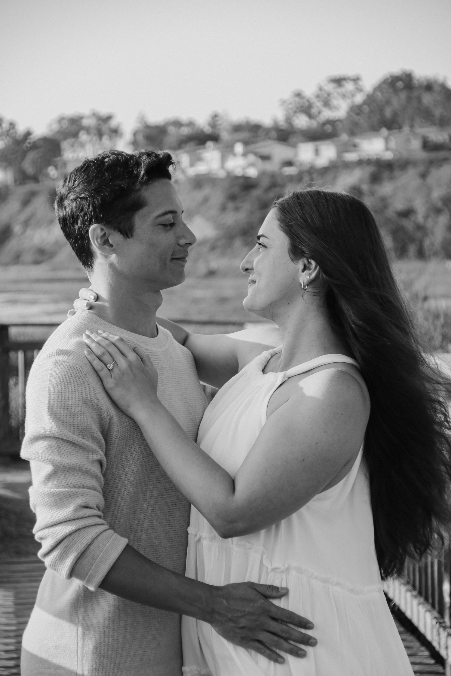 Black and white portrait of a couple embracing on a waterfront boardwalk.