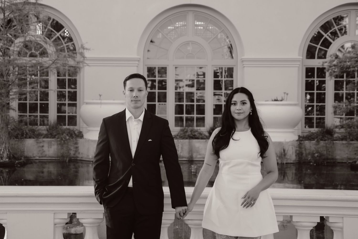 Formal portrait of couple in black and white against elegant architectural backdrop.
