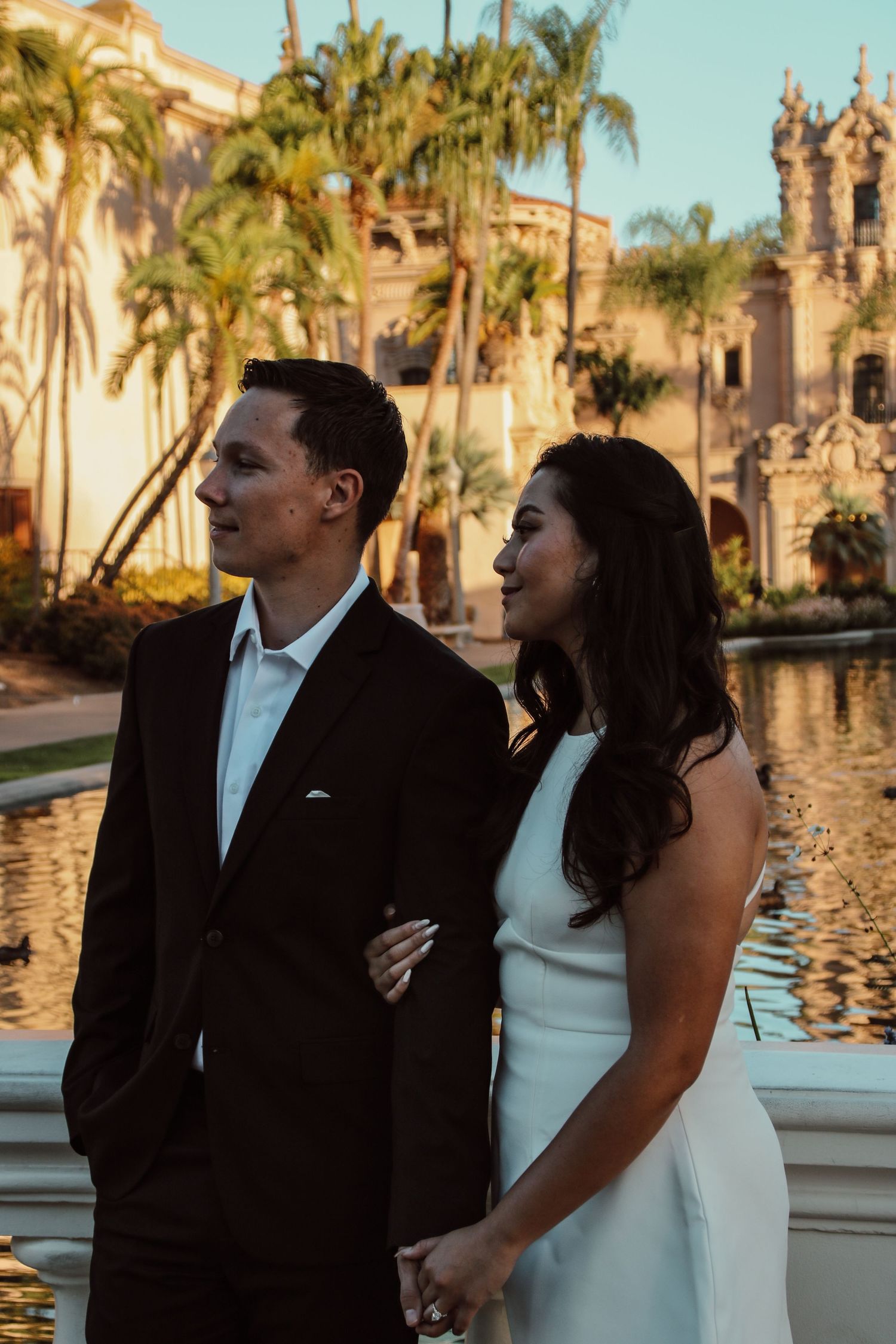Golden hour portrait of formally dressed pair against Spanish colonial building and palm trees.
