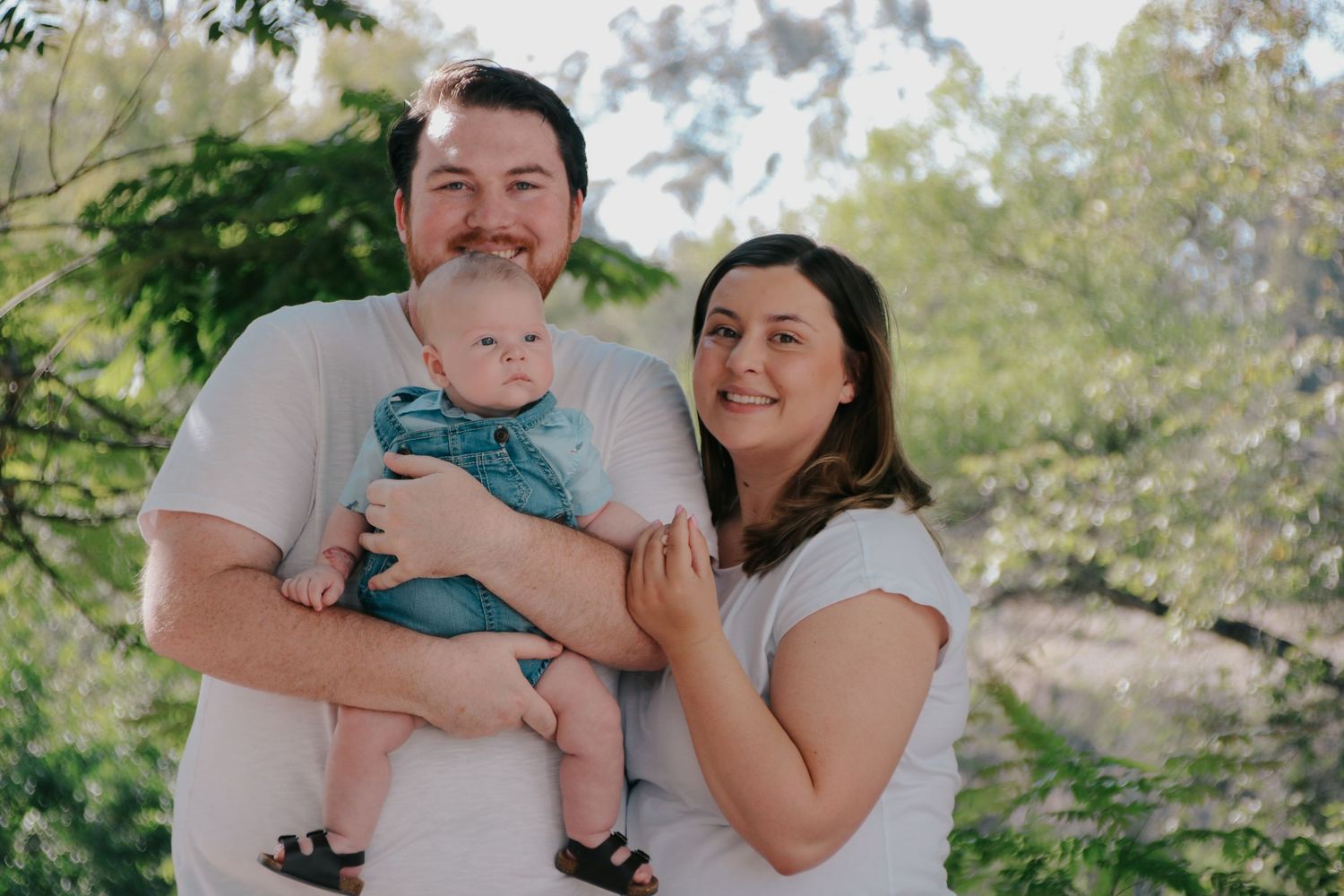 A heartwarming family portrait series showing playful moments between parents and their baby in an outdoor setting.