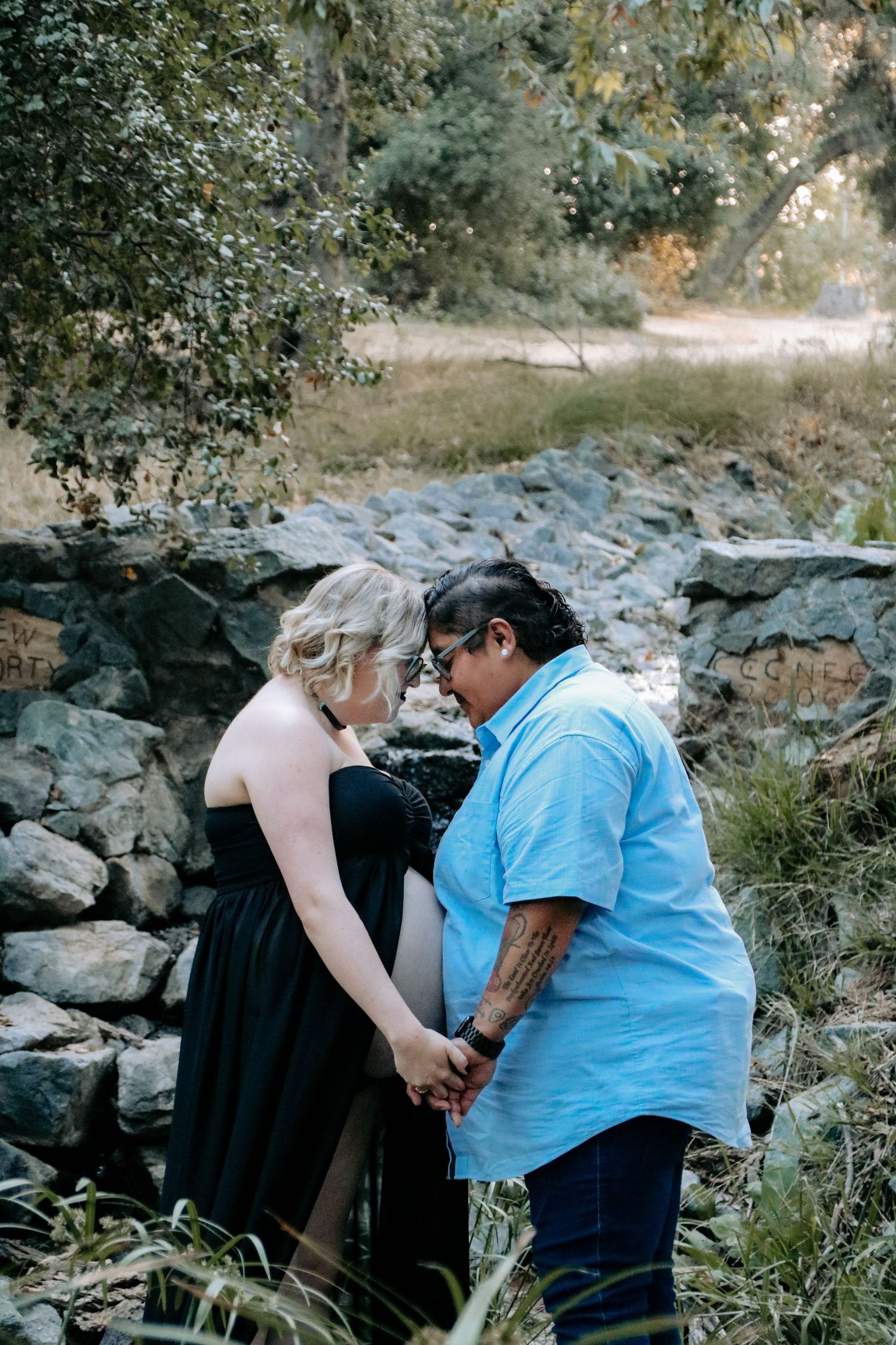 An intimate maternity moment photographed among rocky terrain and greenery in natural lighting.