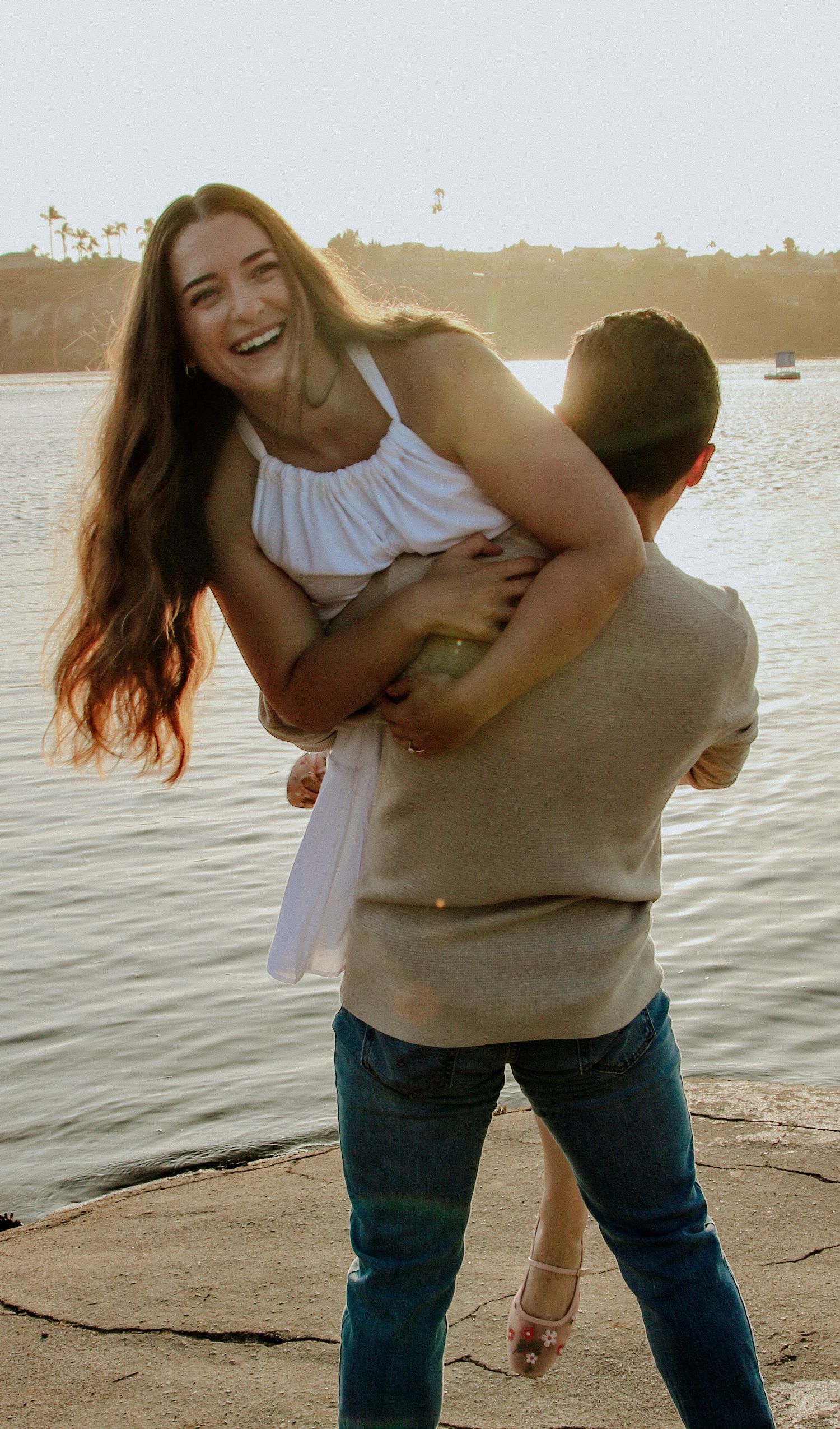 A couple shares laughter during a sunset photoshoot by the water.
