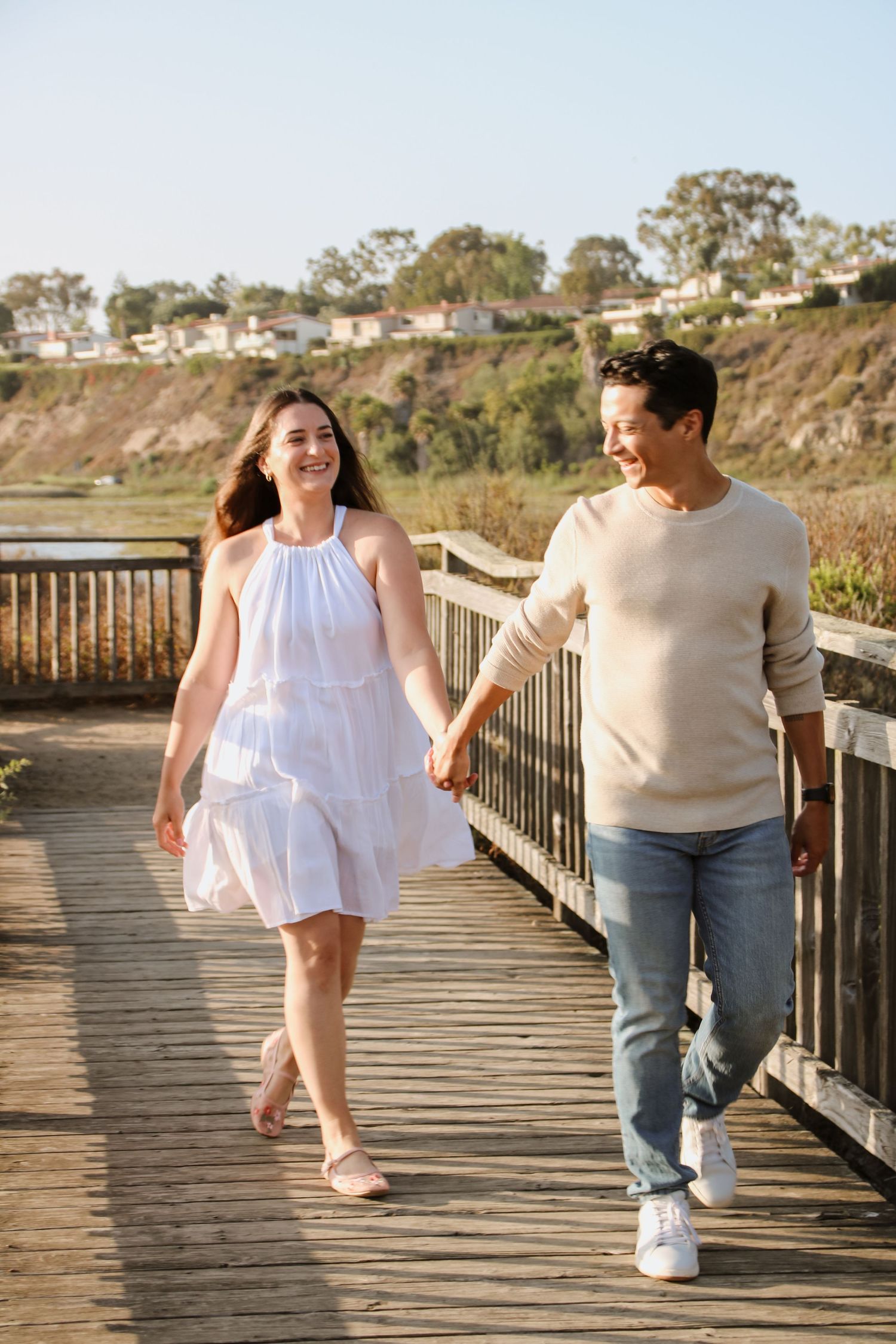 Two people walking hand in hand on a wooden boardwalk with coastal scenery.